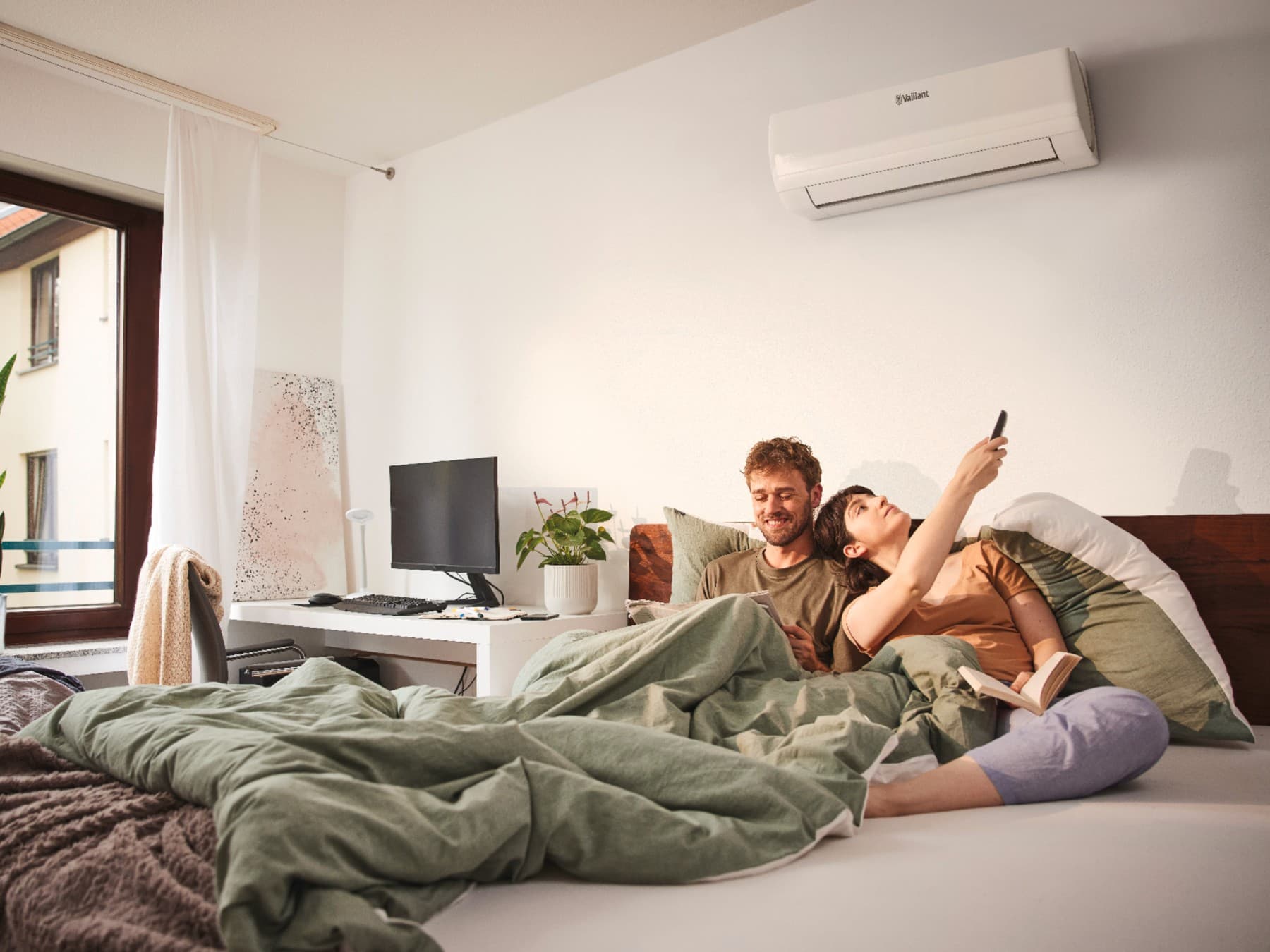 Un couple est au lit et règle leur climatisation avec une télécommande | Vaillant