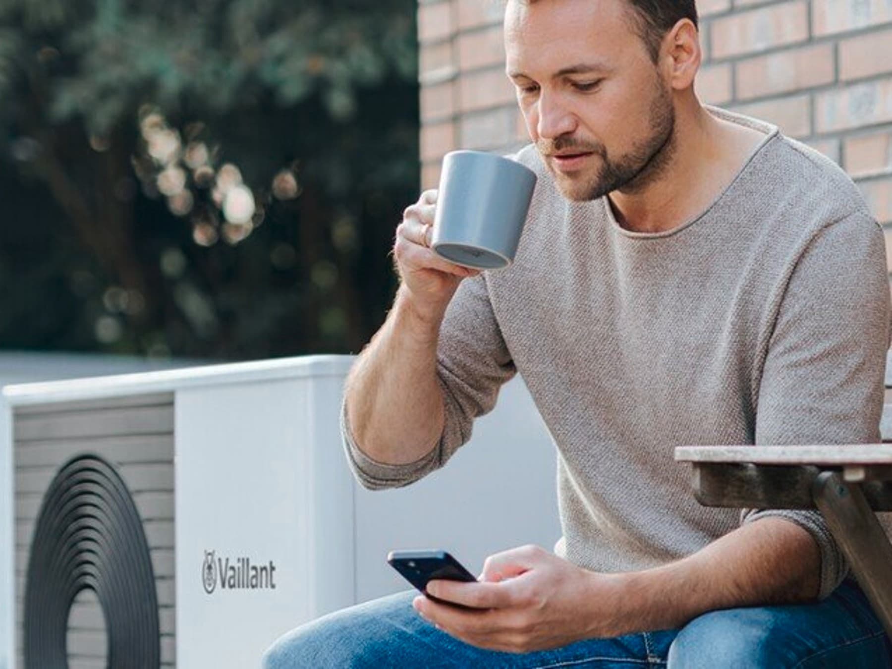 Un homme dans son jardin en train de boire son café devant son portable et le logo EDF | Vaillant