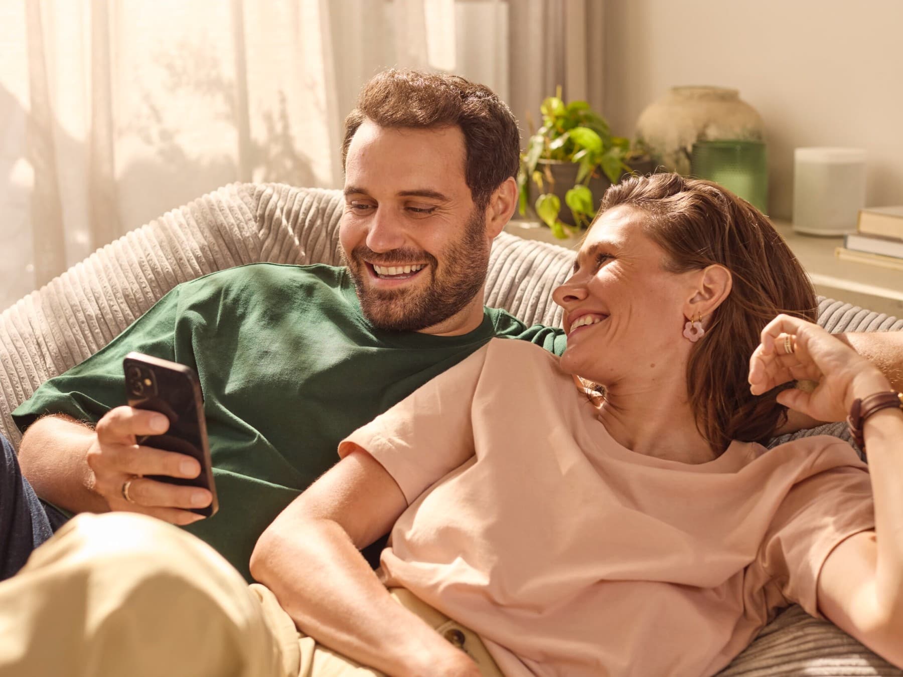 Couple assis sur le canapé vérifiant sa consommation d'énergie sur une application | Vaillant