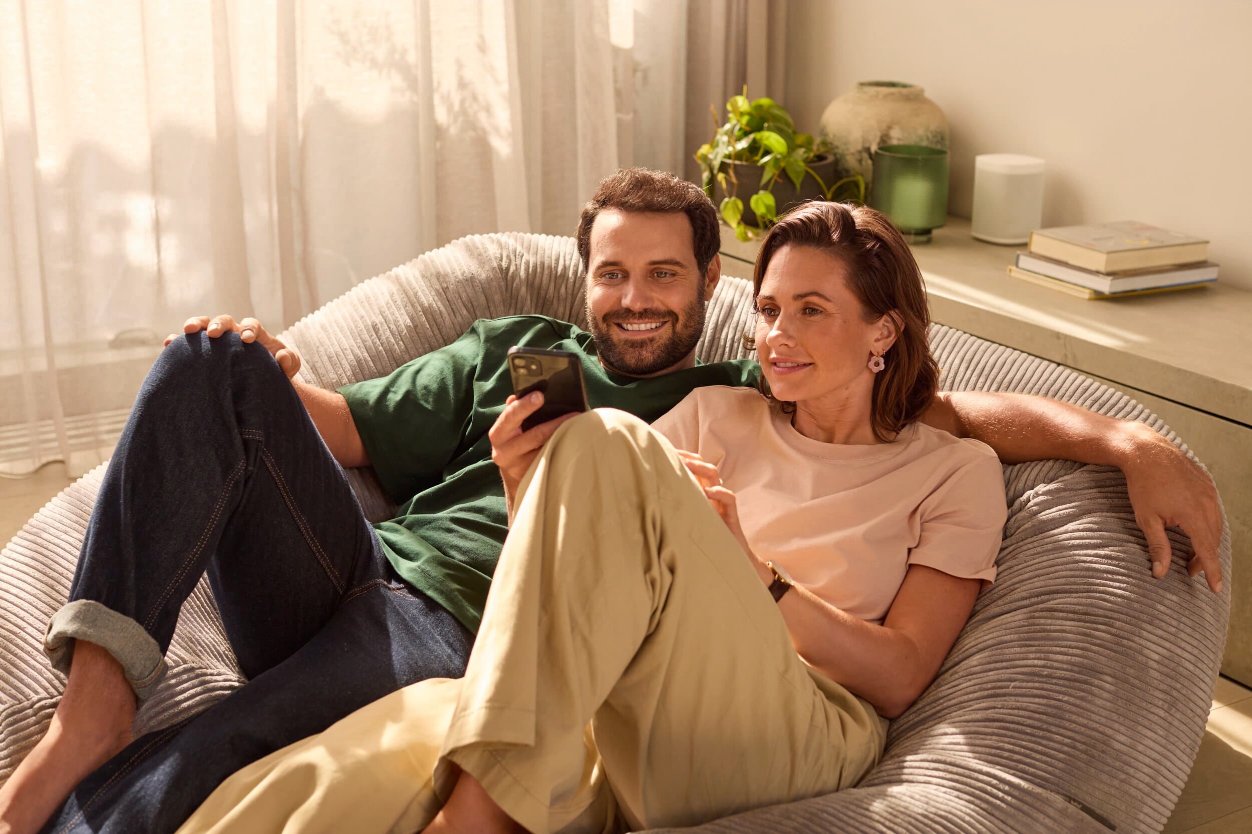 Couple installé dans leur salon consultant leur consommation d'énergie depuis leur téléphone | Vaillant
