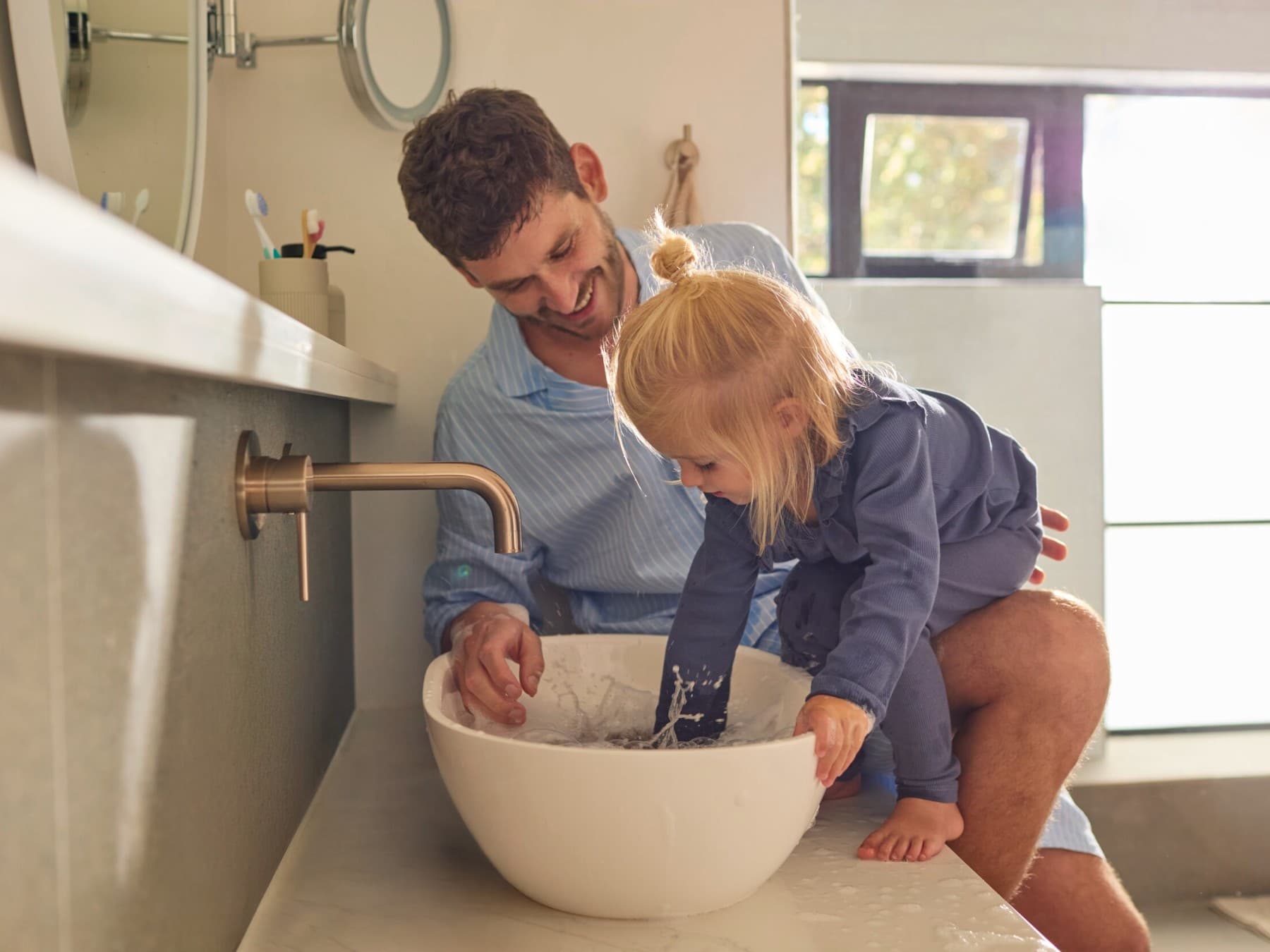 Le père et la fille sont debout devant un lavabo dans la salle de bain et jouent avec l'eau | Vaillant