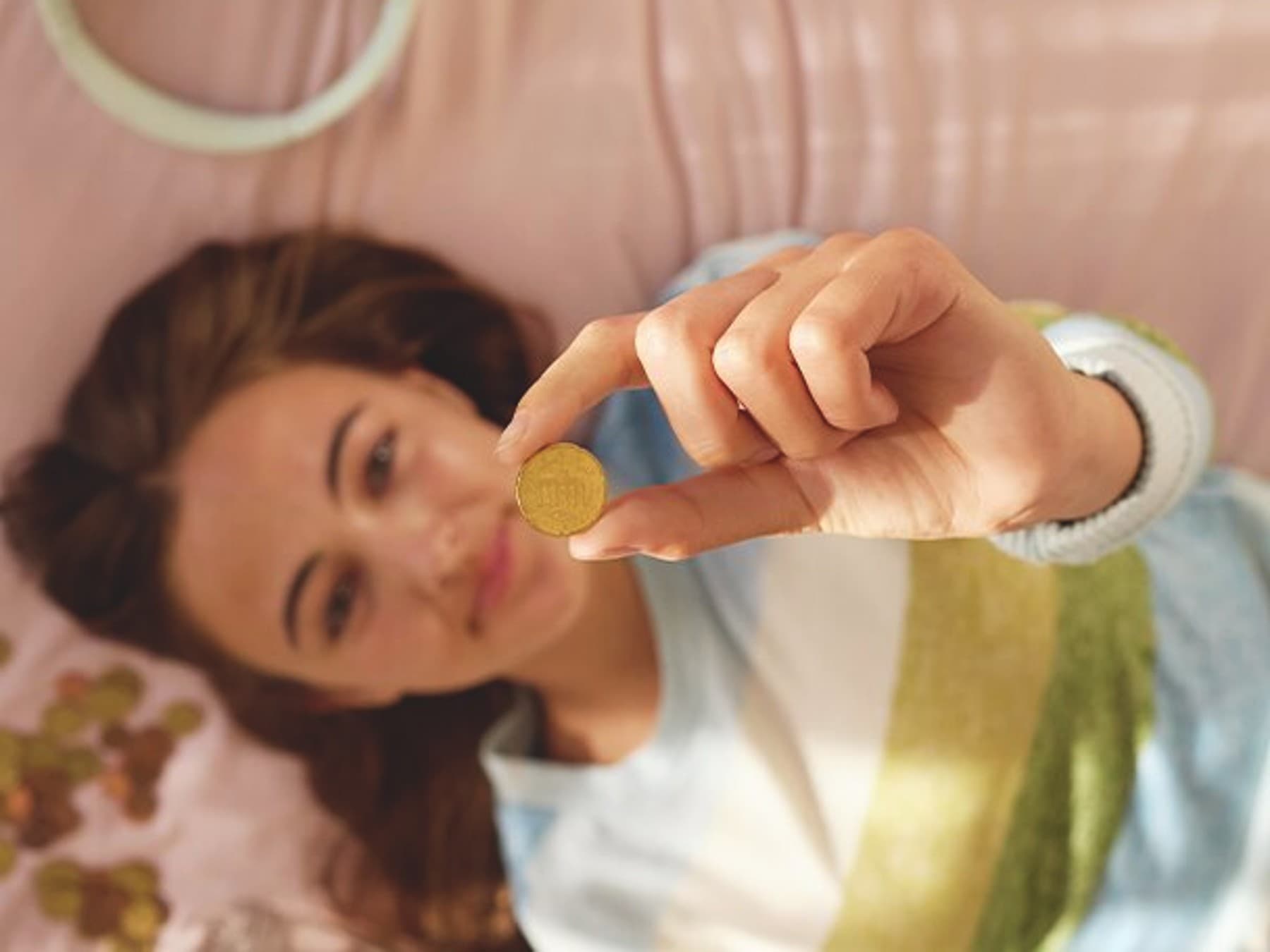 Jeune femme allongée sur un lit tenant une pièce de monnaie en l'air | Vaillant