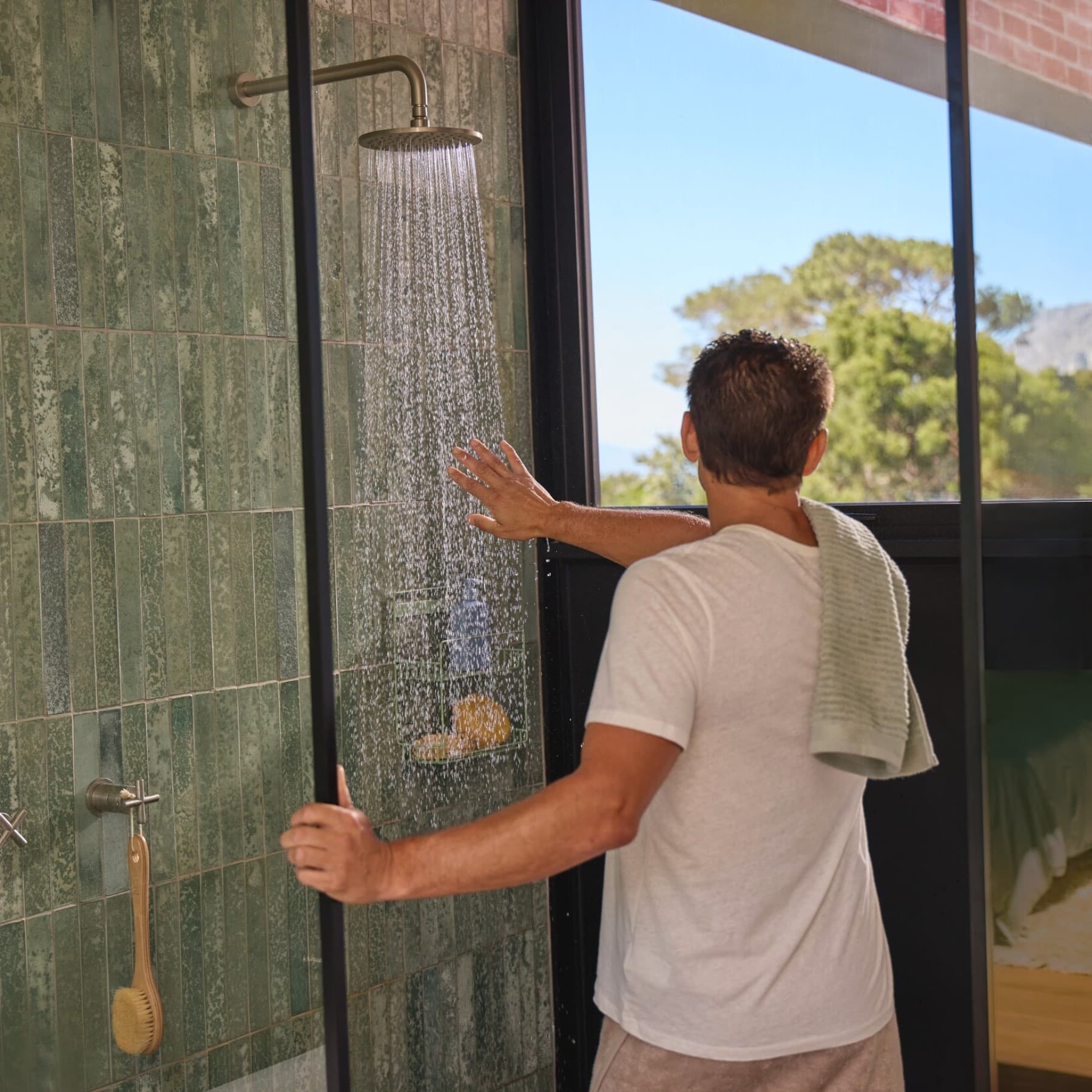 Homme vu de dos tendant la main pour tester la température de l'eau qui coule de la douche | Vaillant