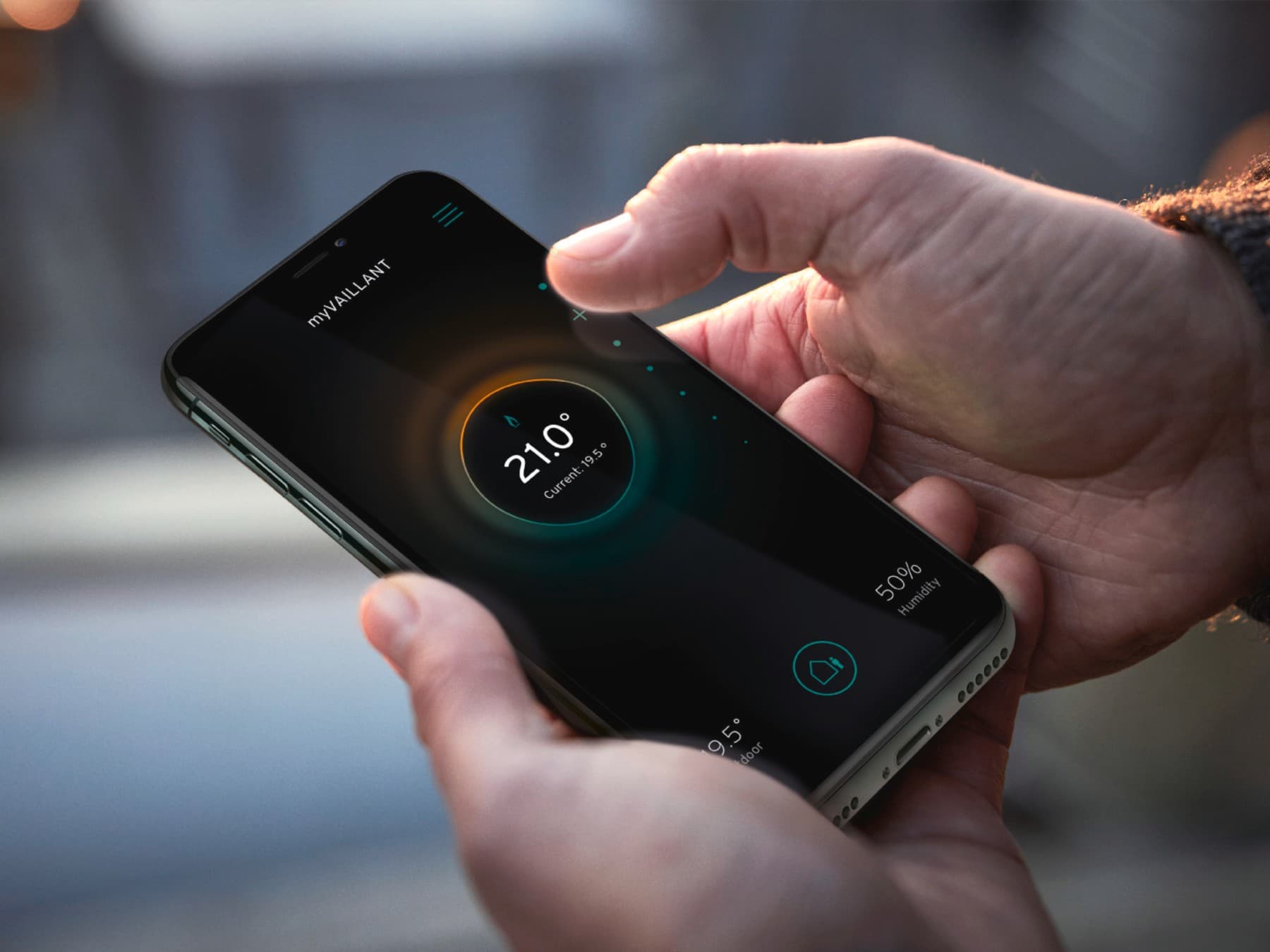 Homme tenant son smartphone dans sa main pour contrôler son thermostat à distance | Vaillant