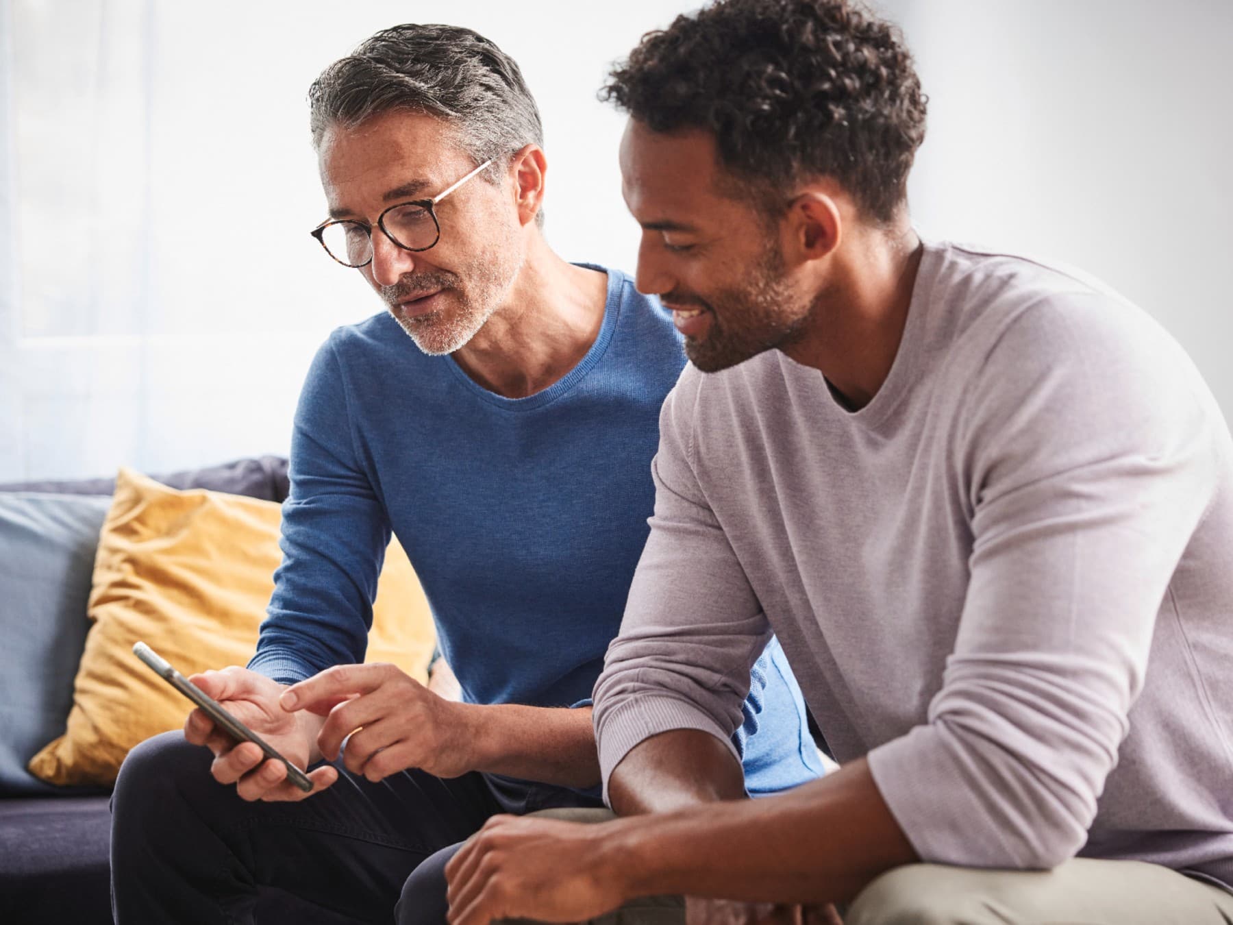Deux hommes assis sur un canapé explore le glossaire du chauffage sur leur smartphone | Vaillant
