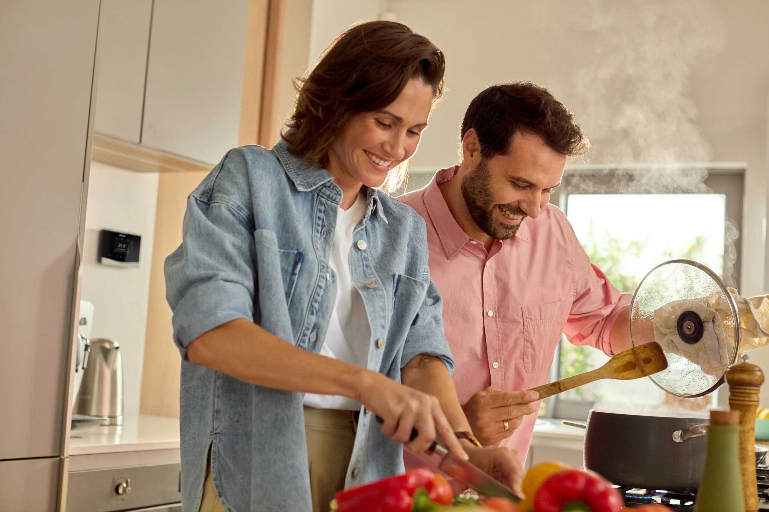 Couple préparent à manger avec sensoHOME accroché sur le mur de leur cuisine | Vaillant