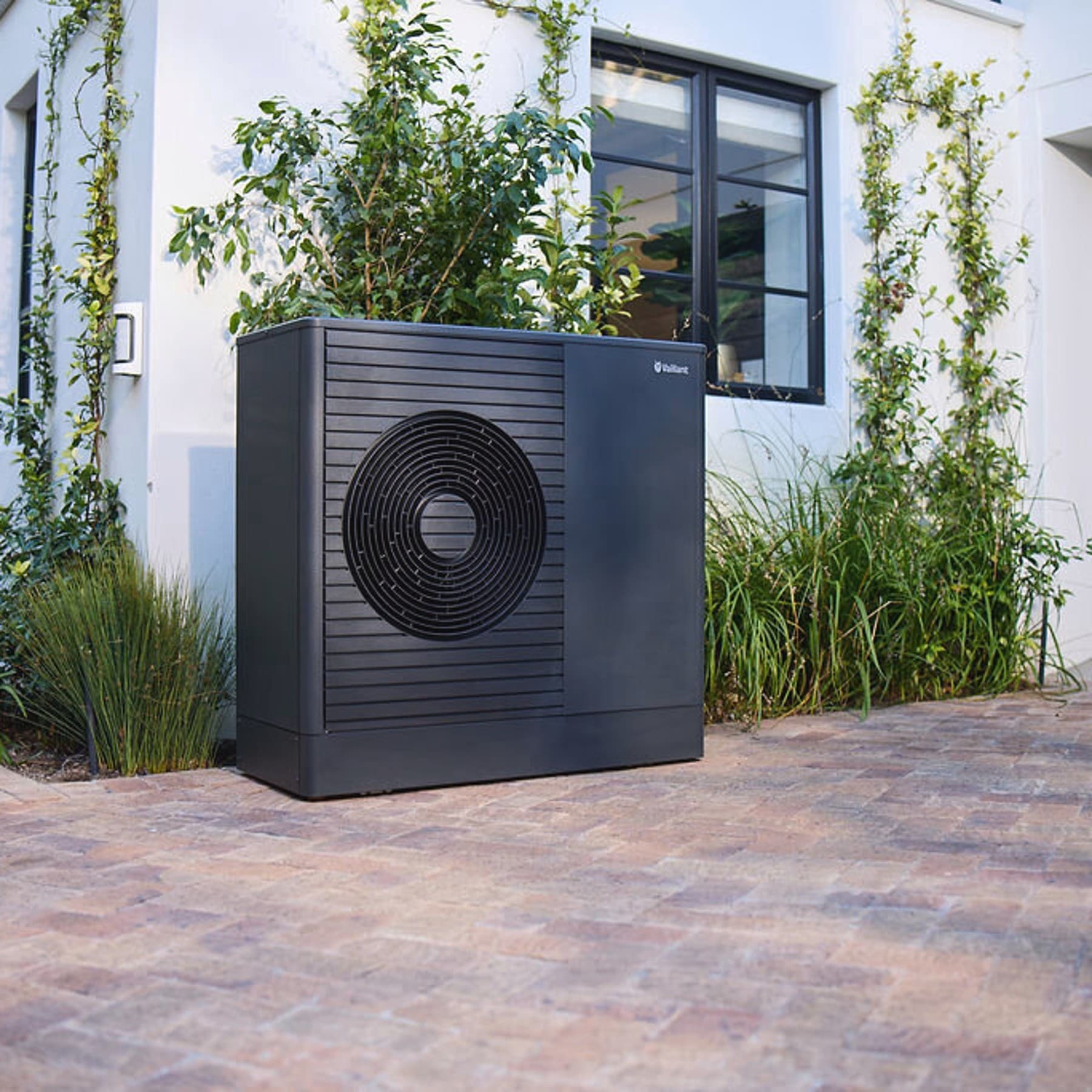 Pompe à chaleur aroTHERM plus dans le jardin devant une maison | Vaillant