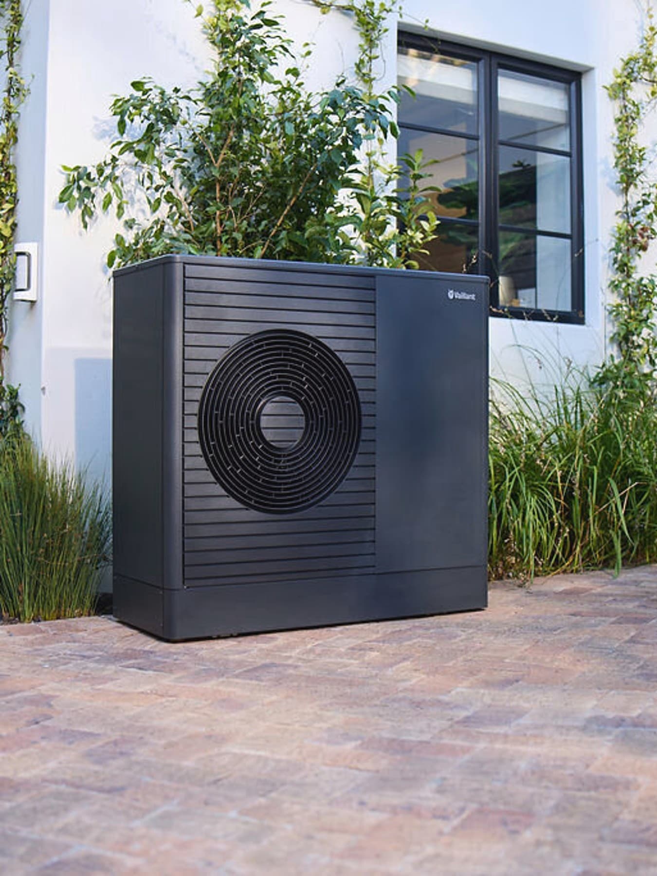 Pompe à chaleur aroTHERM plus dans le jardin devant une maison | Vaillant