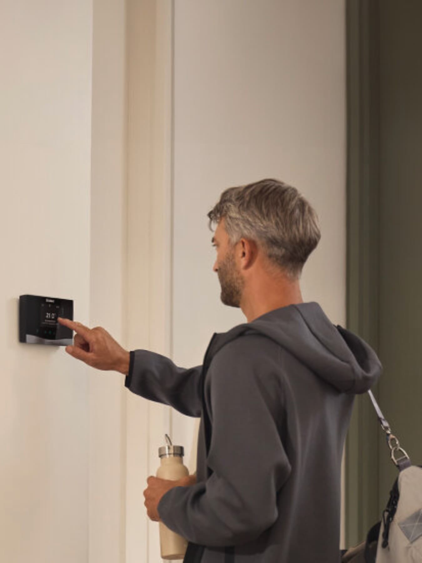 Une personne qui règle les paramètres d'un thermostat fixé au mur | Vaillant