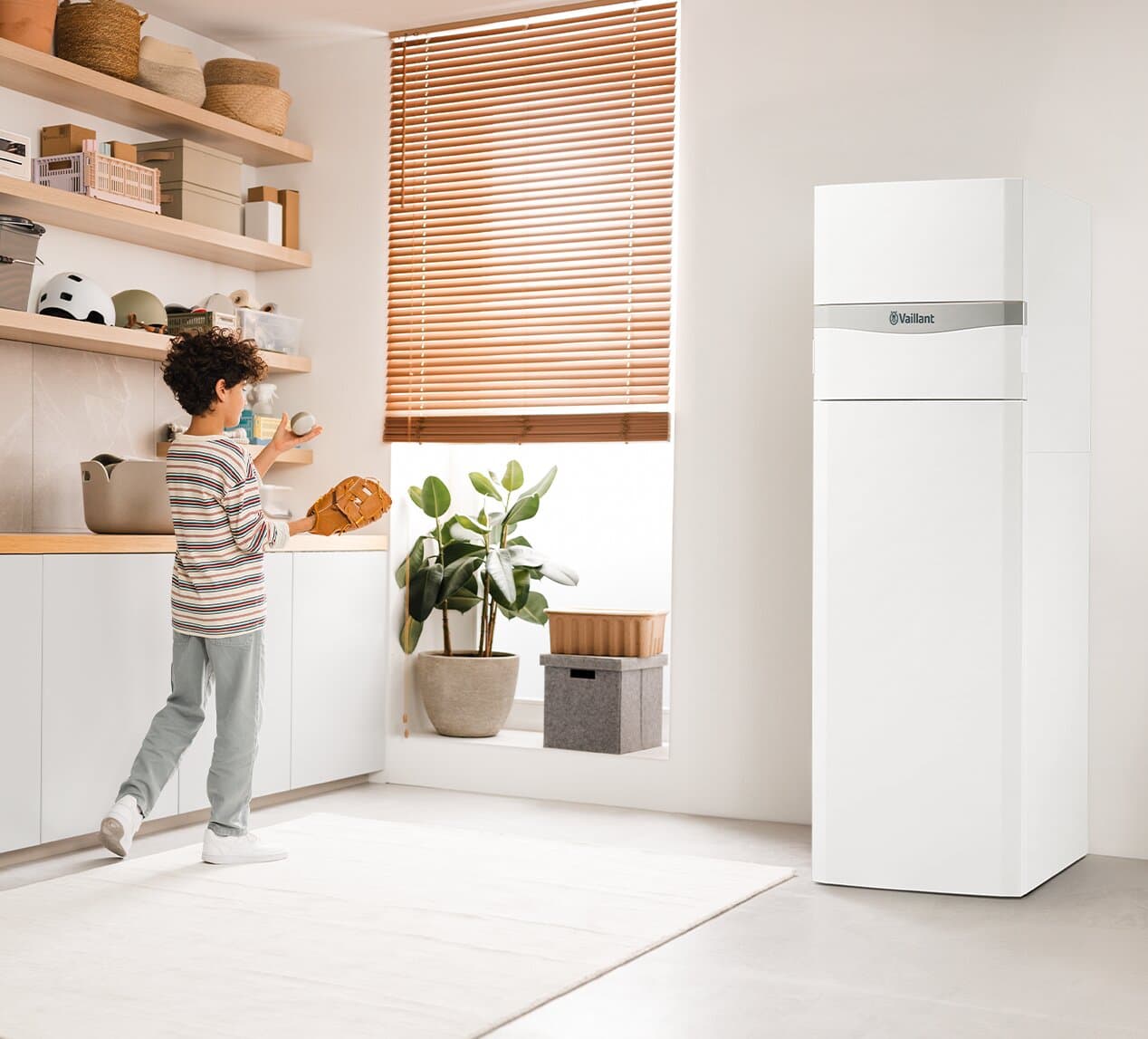 Un garçon joue dans une buanderie à côté de la pompe à chaleur flexoCOMPACT exclusive | Vaillant