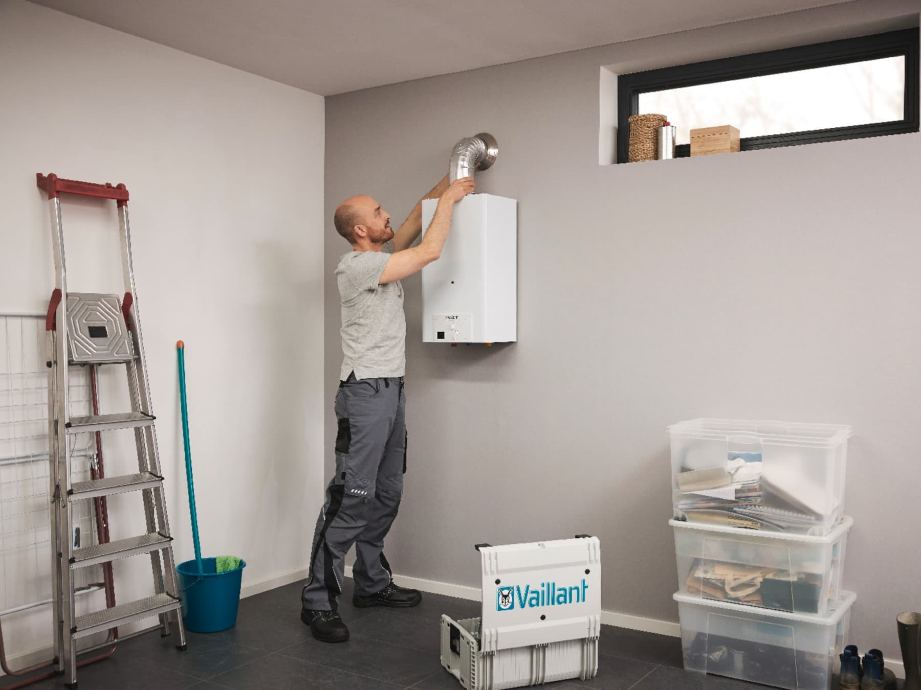 Un installateur finit l'installation d'un chauffe-eau gaz dans un garage | Vaillant