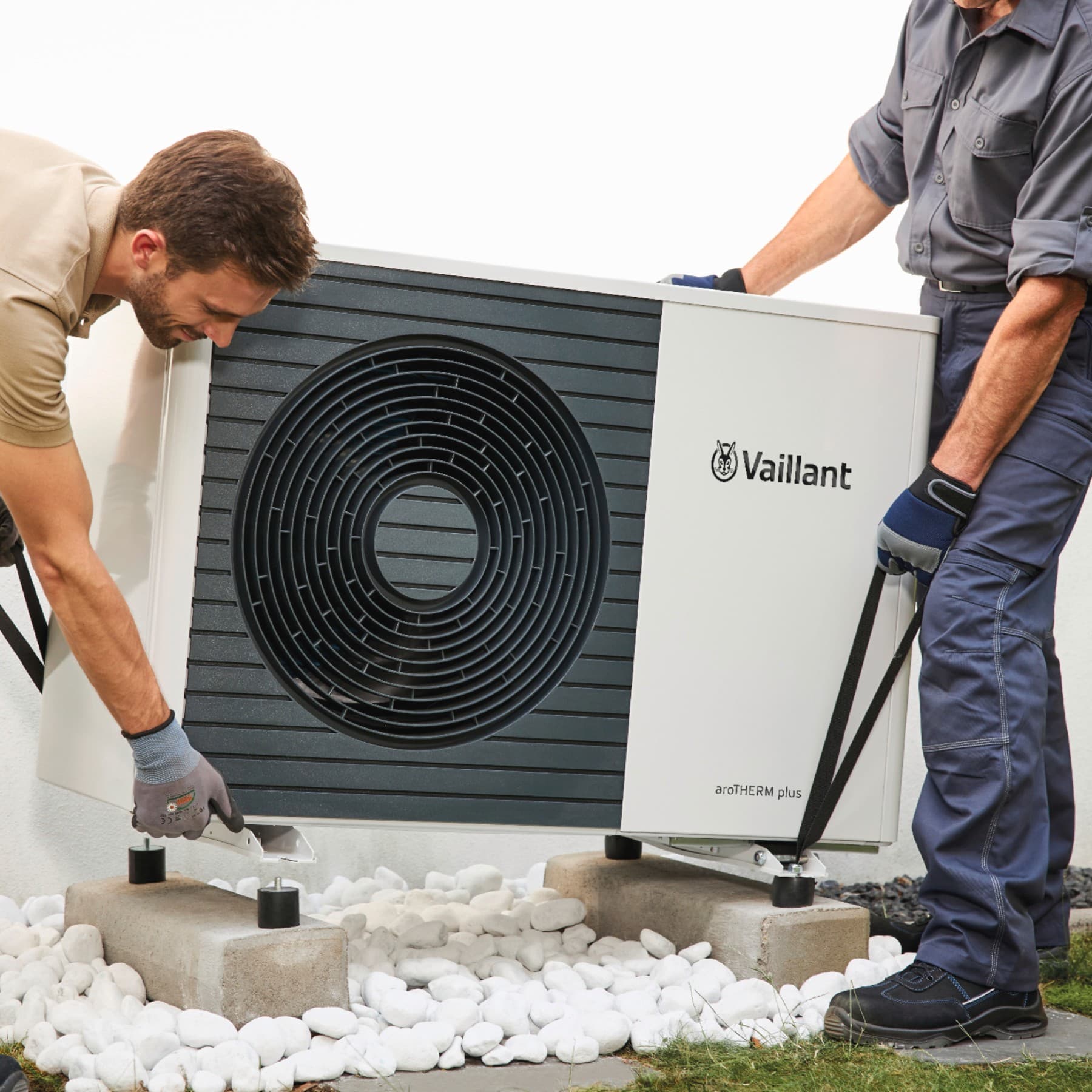 Deux installateurs posent une unité extérieure de pompe à chaleur sur une terrasse | Vaillant