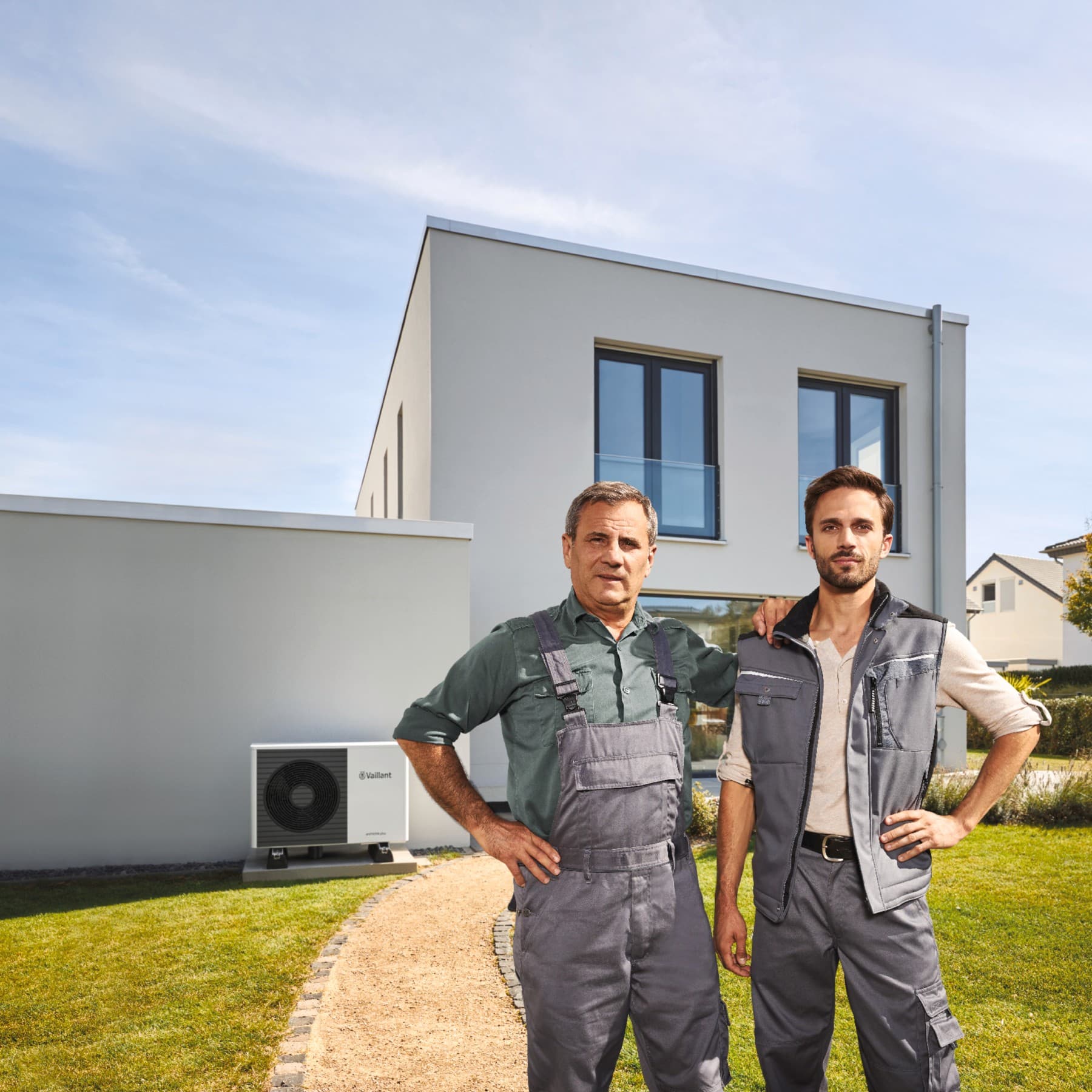 2 artisans RGE qui posent devant une maison avec une pompe à chaleur | Vaillant