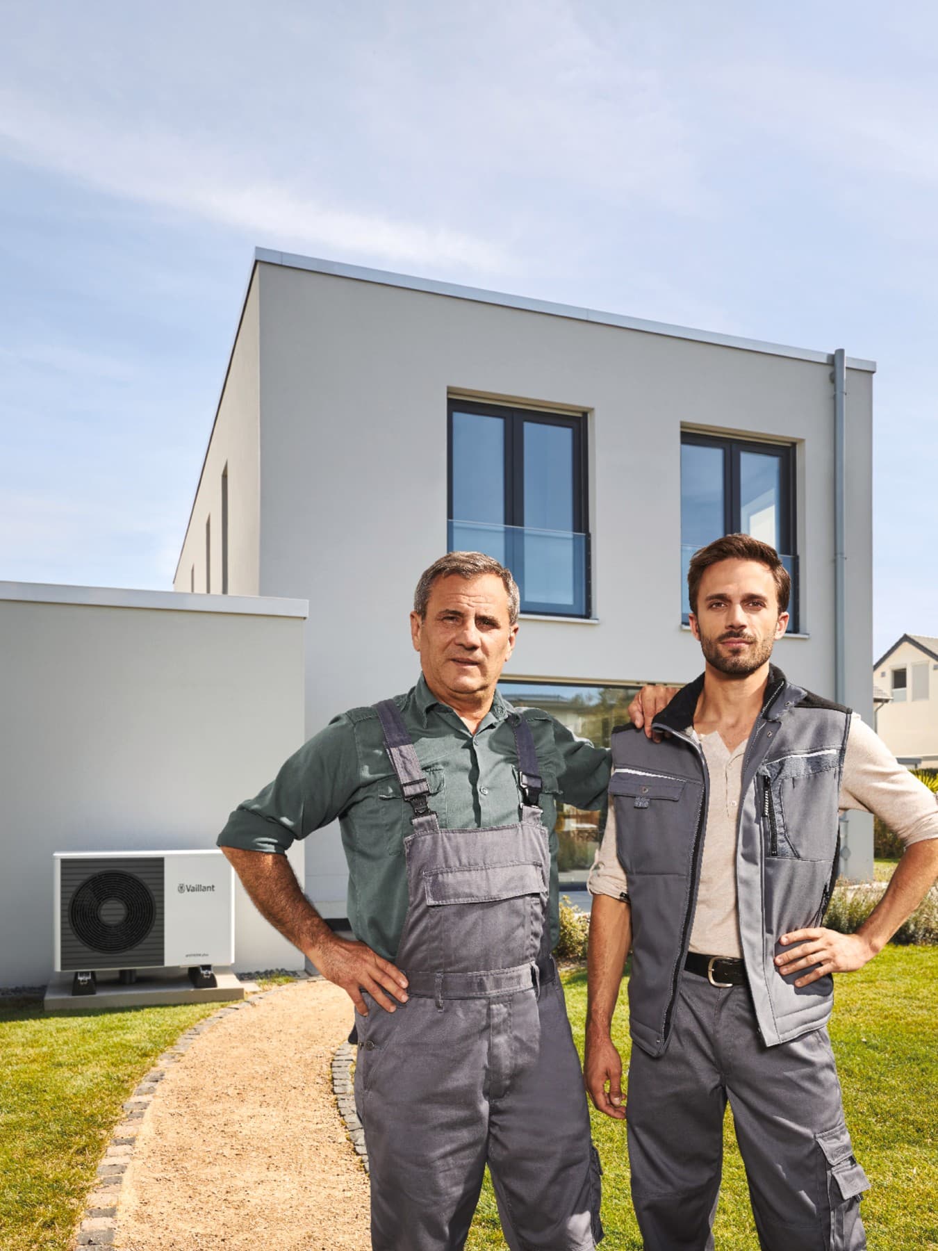 2 artisans RGE qui posent devant une maison avec une pompe à chaleur | Vaillant