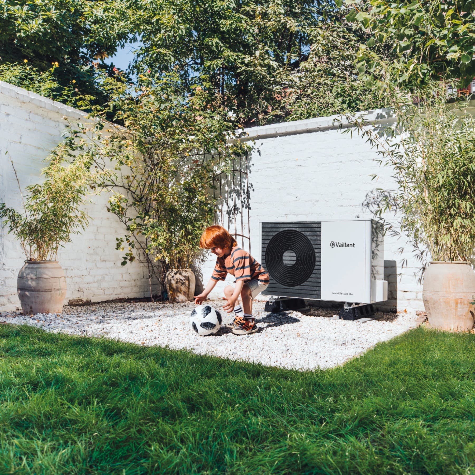 Enfant jouant au football dans le jardin devant une pompe à chaleur | Vaillant