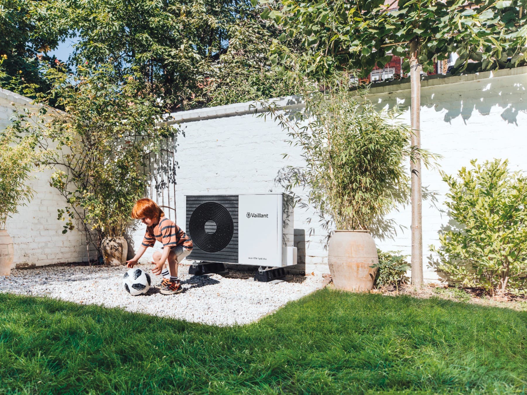 Enfant jouant au football dans le jardin devant une pompe à chaleur | Vaillant
