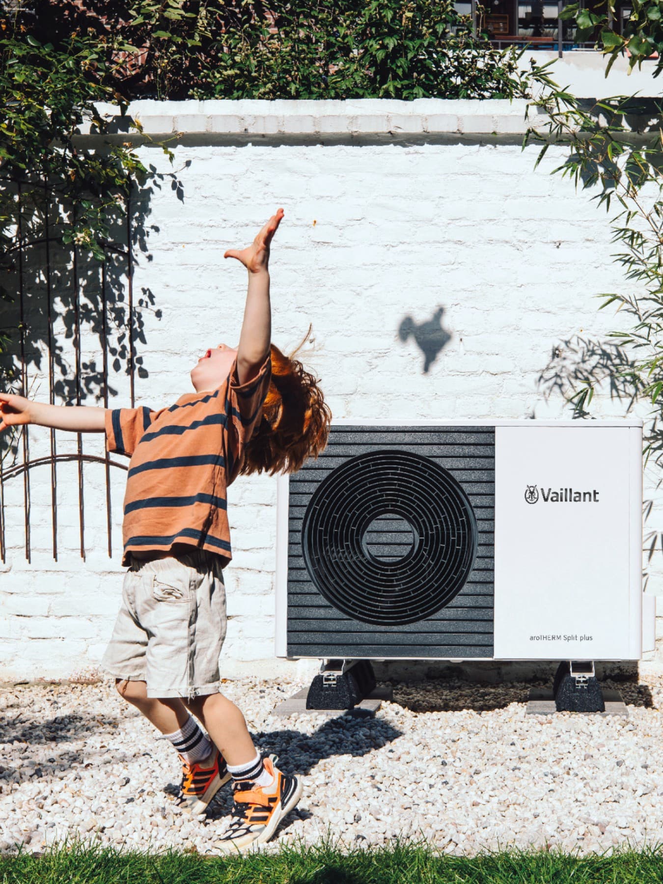 Un jeune garçon joue dans le jardin devant une unité extérieure de pompe à chaleur | Vaillant