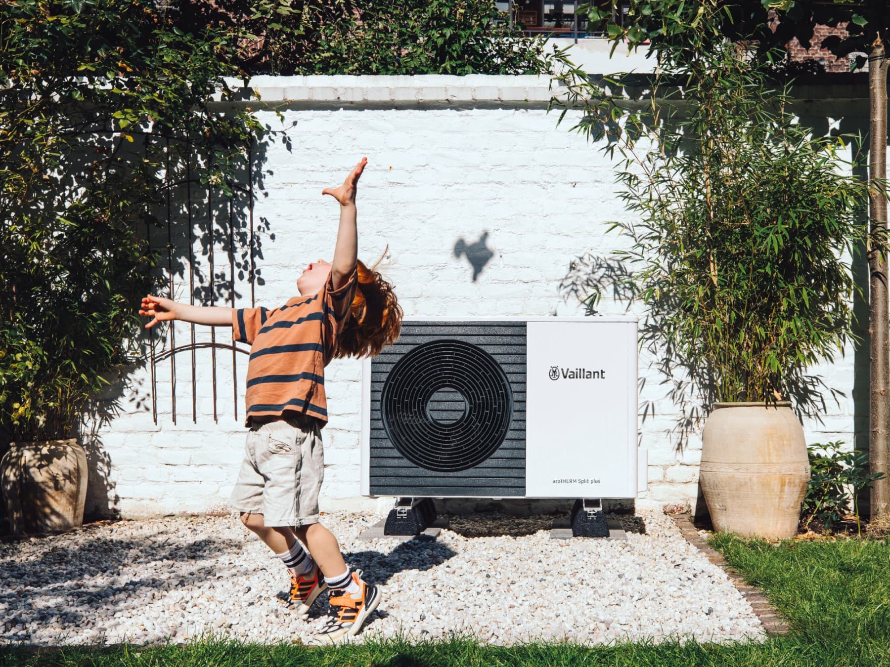 Enfant jouant au football dans le jardin devant une pompe à chaleur | Vaillant