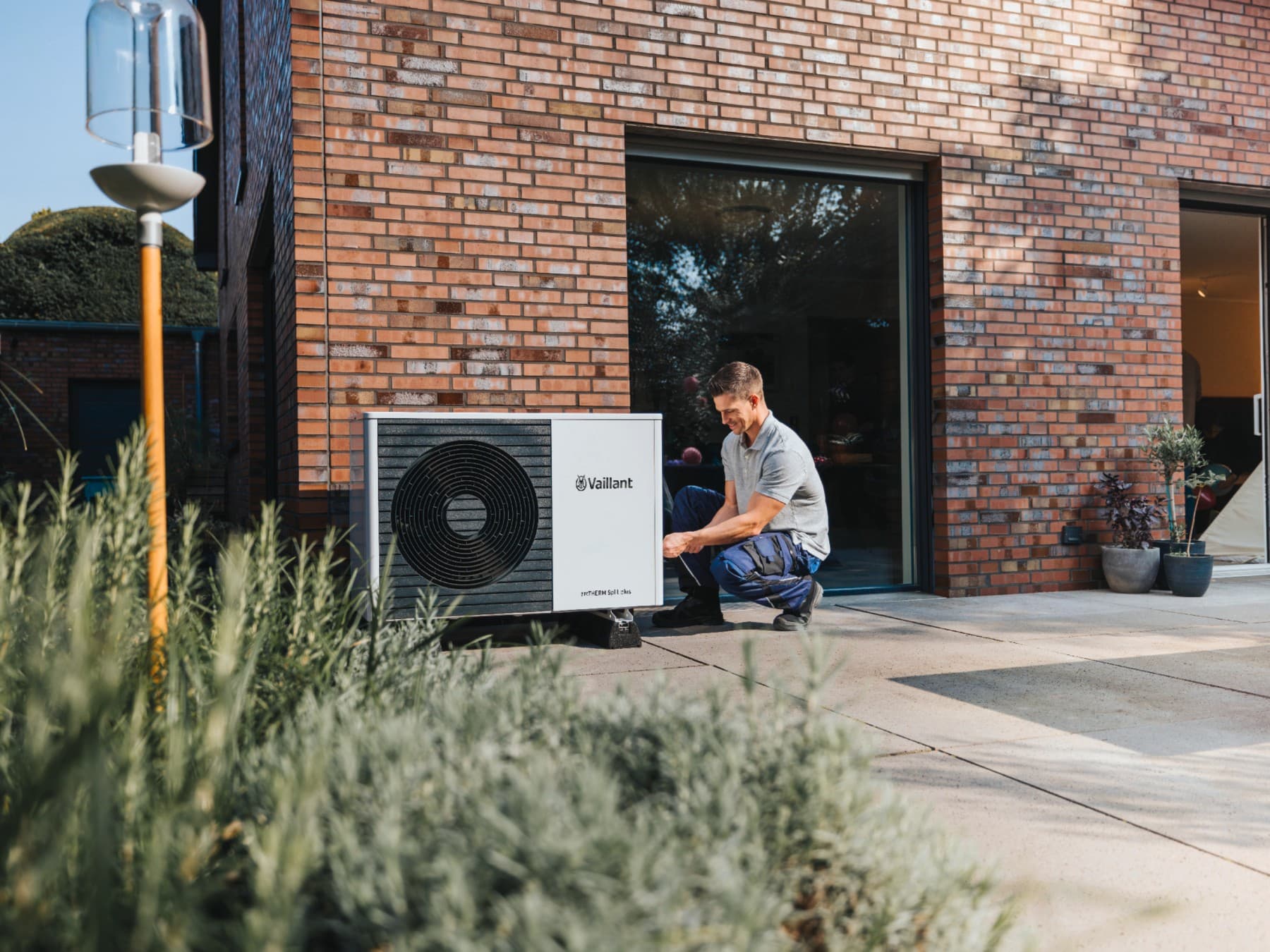 Installateur avec une pompe à chaleur devant une maison | Vaillant