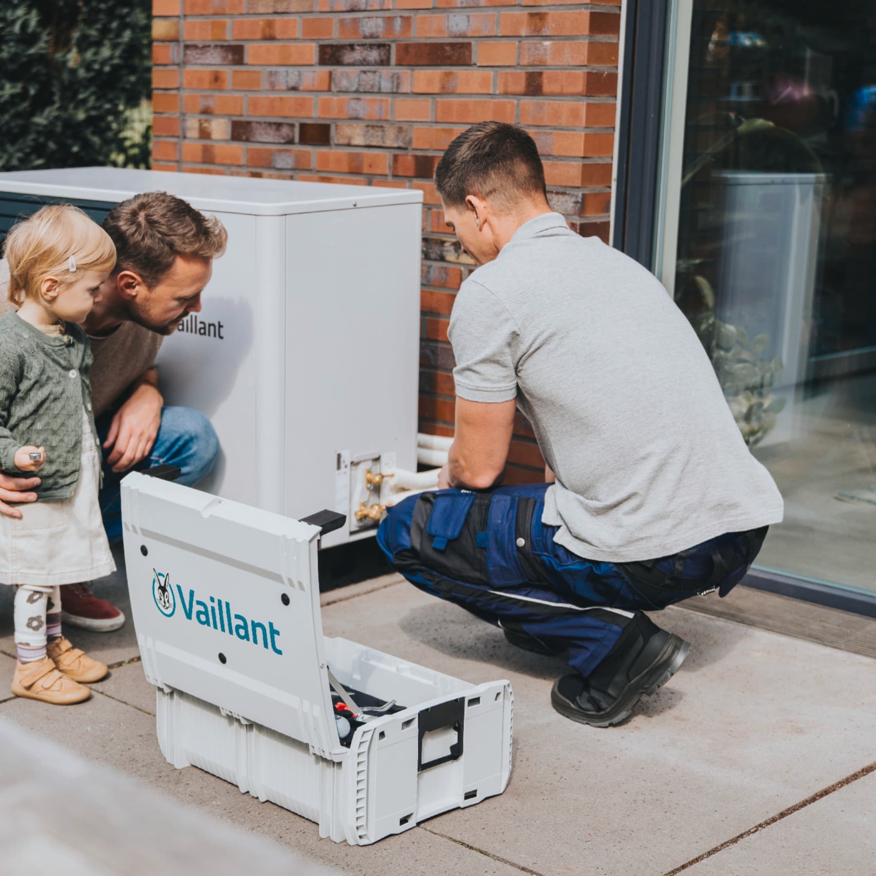 Un père et sa fille regardent un installateur installer une pompe à chaleur | Vaillant
