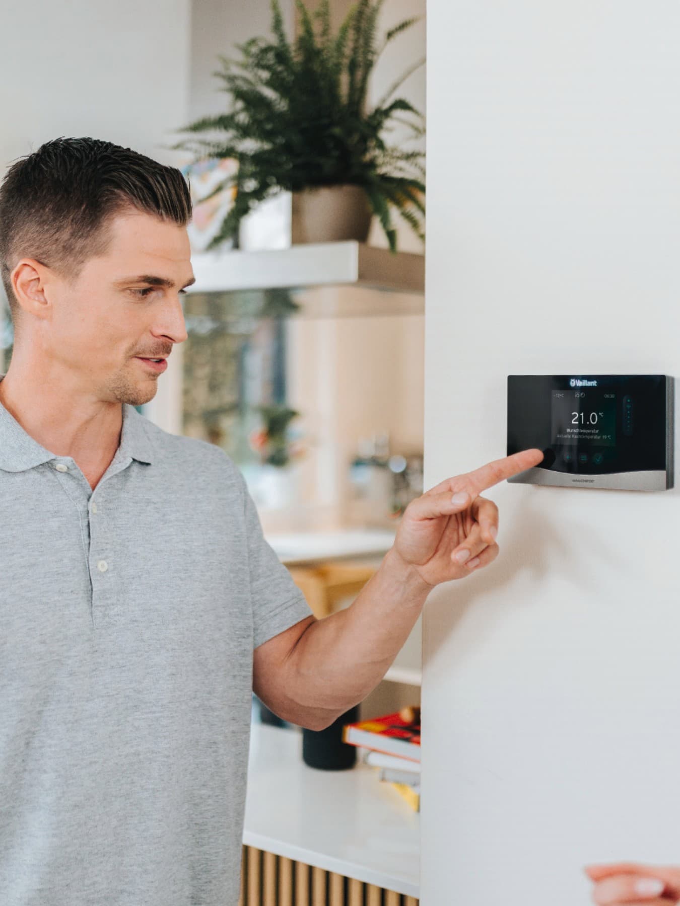 Un homme est au premier plan, la main posée sur un thermostat fixé à un mur bleu | Vaillant
