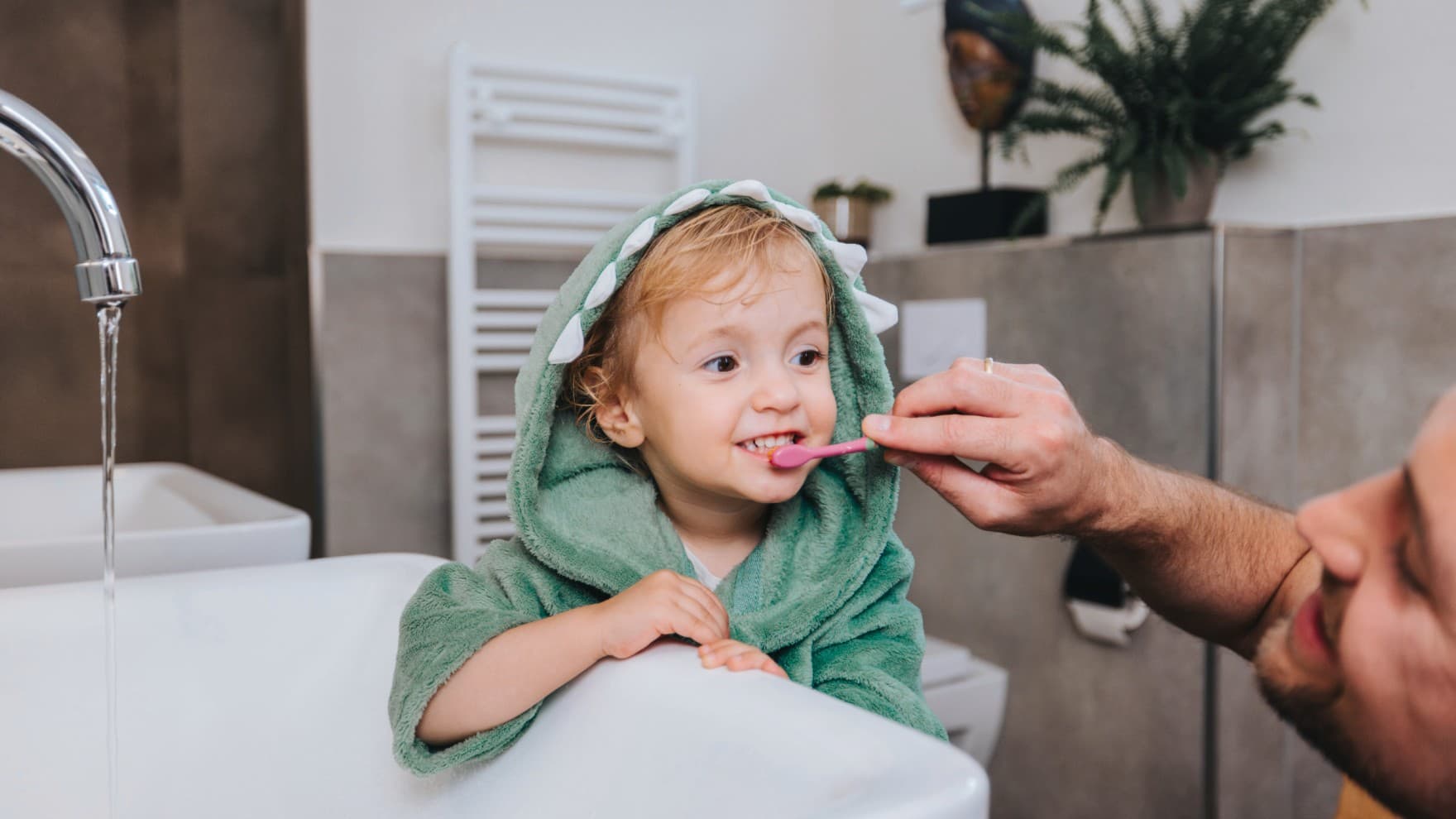 Un père brosse les dents de son enfant avec un sèche-serviettes chauffant en arrière-plan | Vaillant