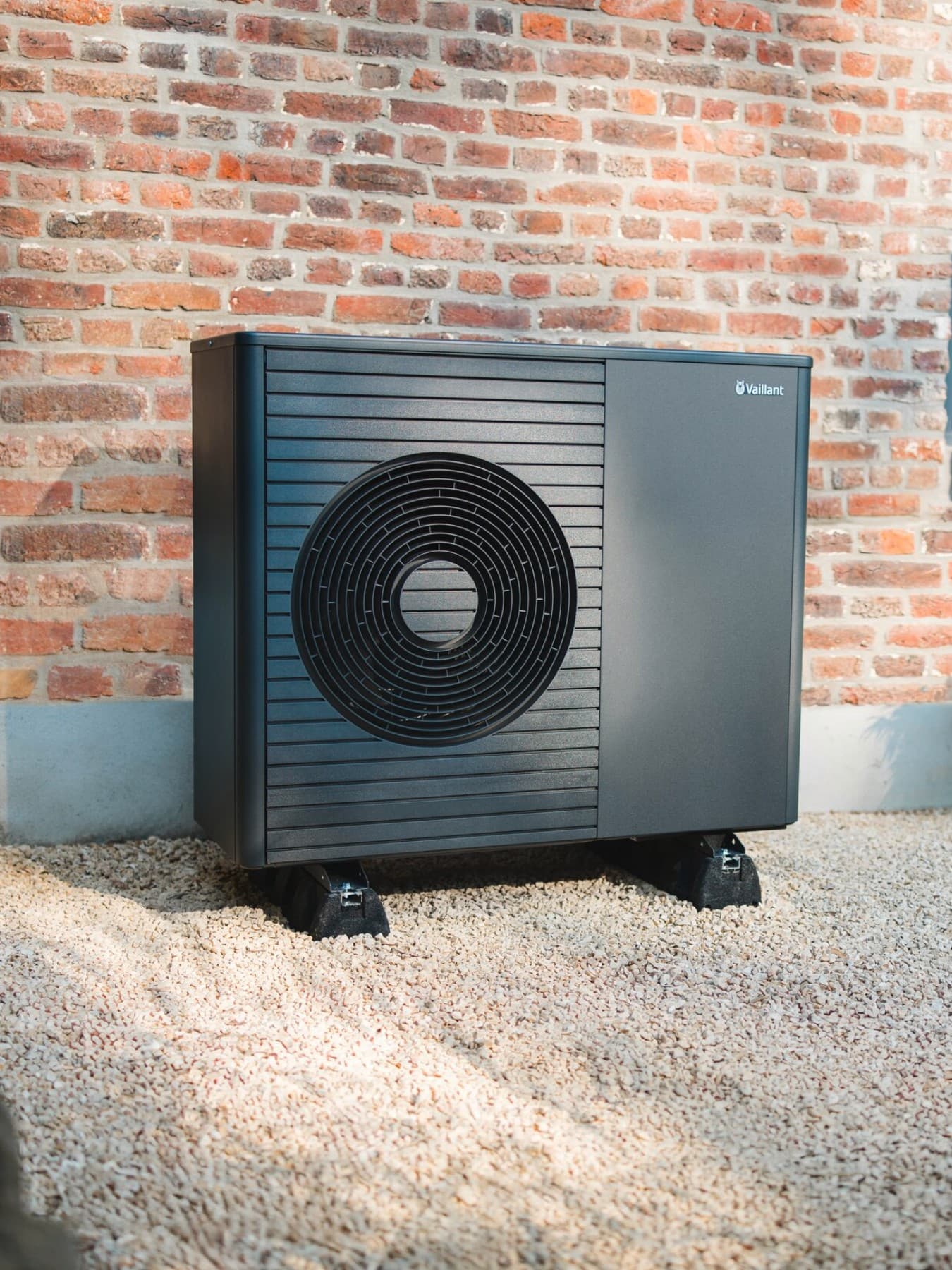 Une pompe à chaleur se trouve devant un bâtiment neuf, avec une pelouse bien entretenue et un chemin au premier plan | Vaillant