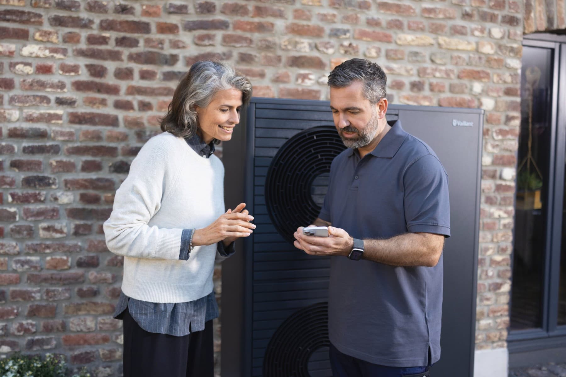 Installateur et propriétaire devant la pompe à chaleur | Vaillant