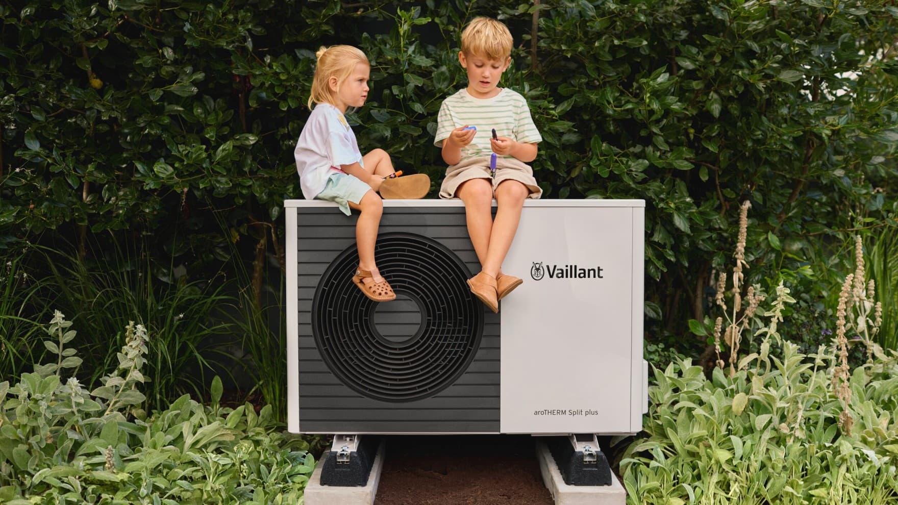 Une pompe à chaleur avec deux enfants assis sur l'unité extérieure | Vaillant