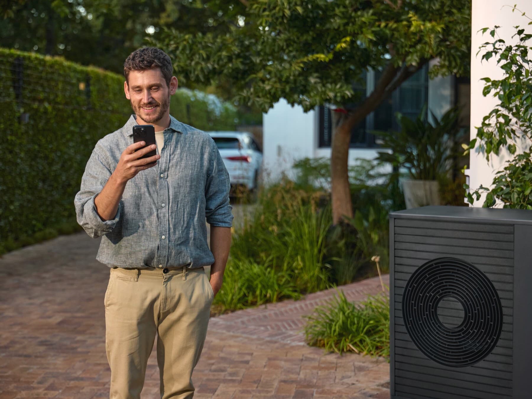 Homme debout à côté d'une pompe à chaleur, regardant un smartphone | Vaillant
