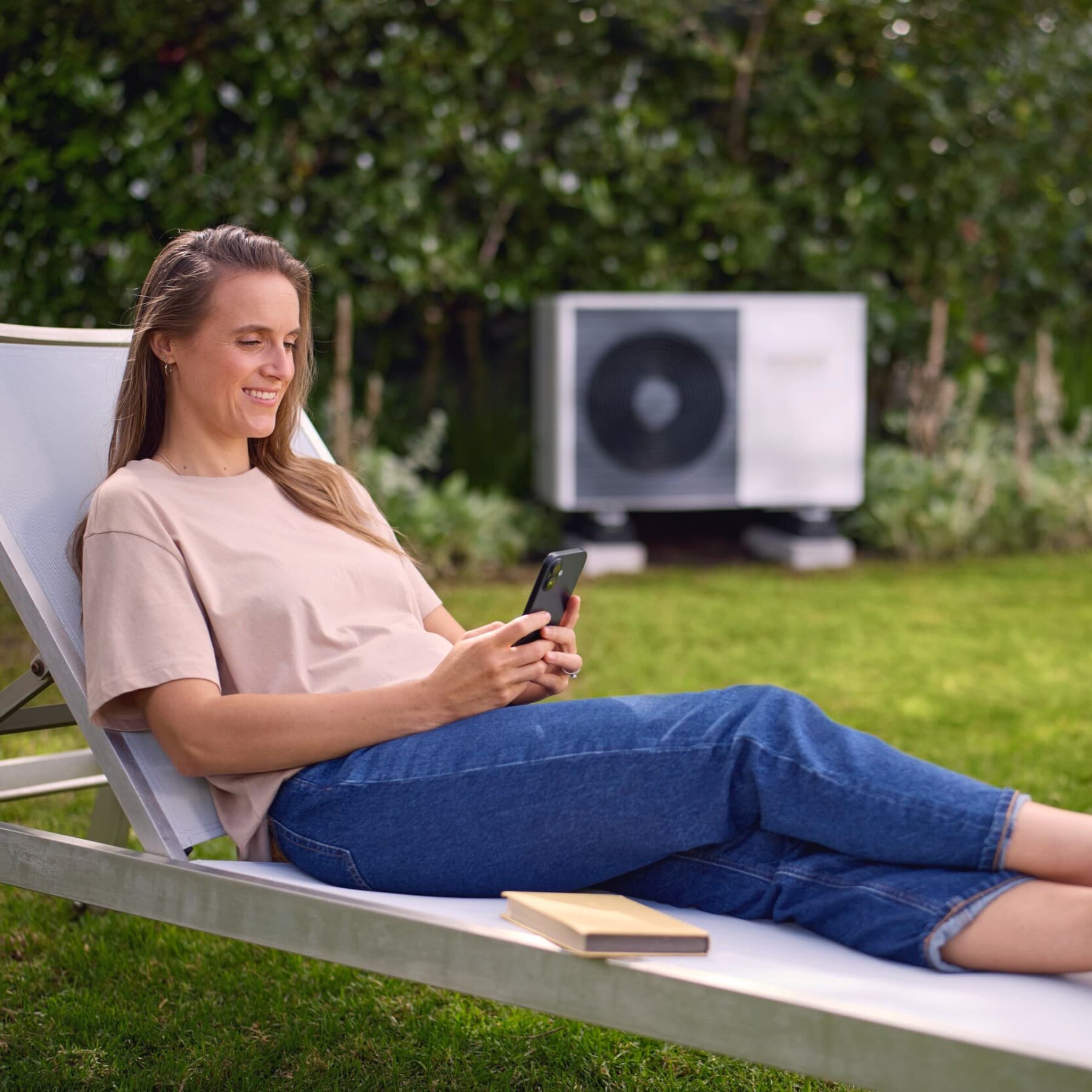 Jeune femme sur un transat dans son jardin avec une unité extérieure de pompe à chaleur air-eau | Vaillant
