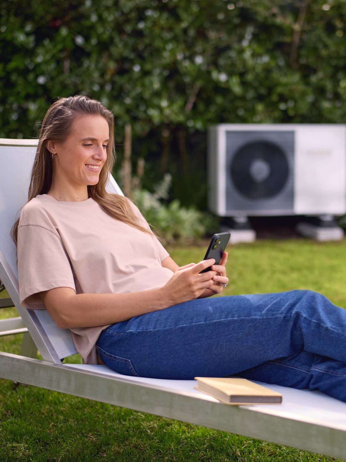 Jeune femme sur un transat dans son jardin avec une unité extérieure de pompe à chaleur air-eau | Vaillant
