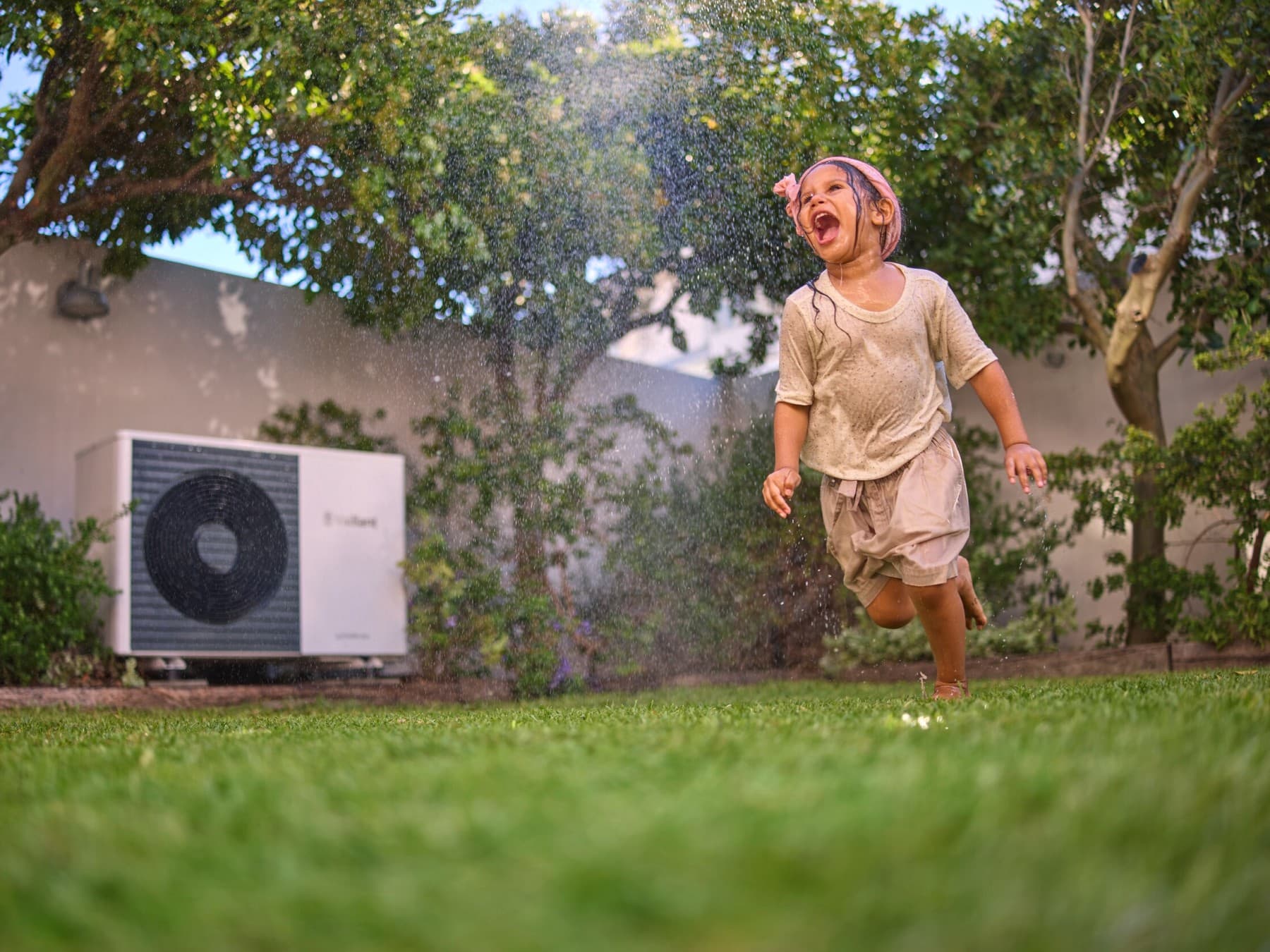 Une petite fille jouant dans son jardin avec une pompe à chaleur en fond | Vaillant