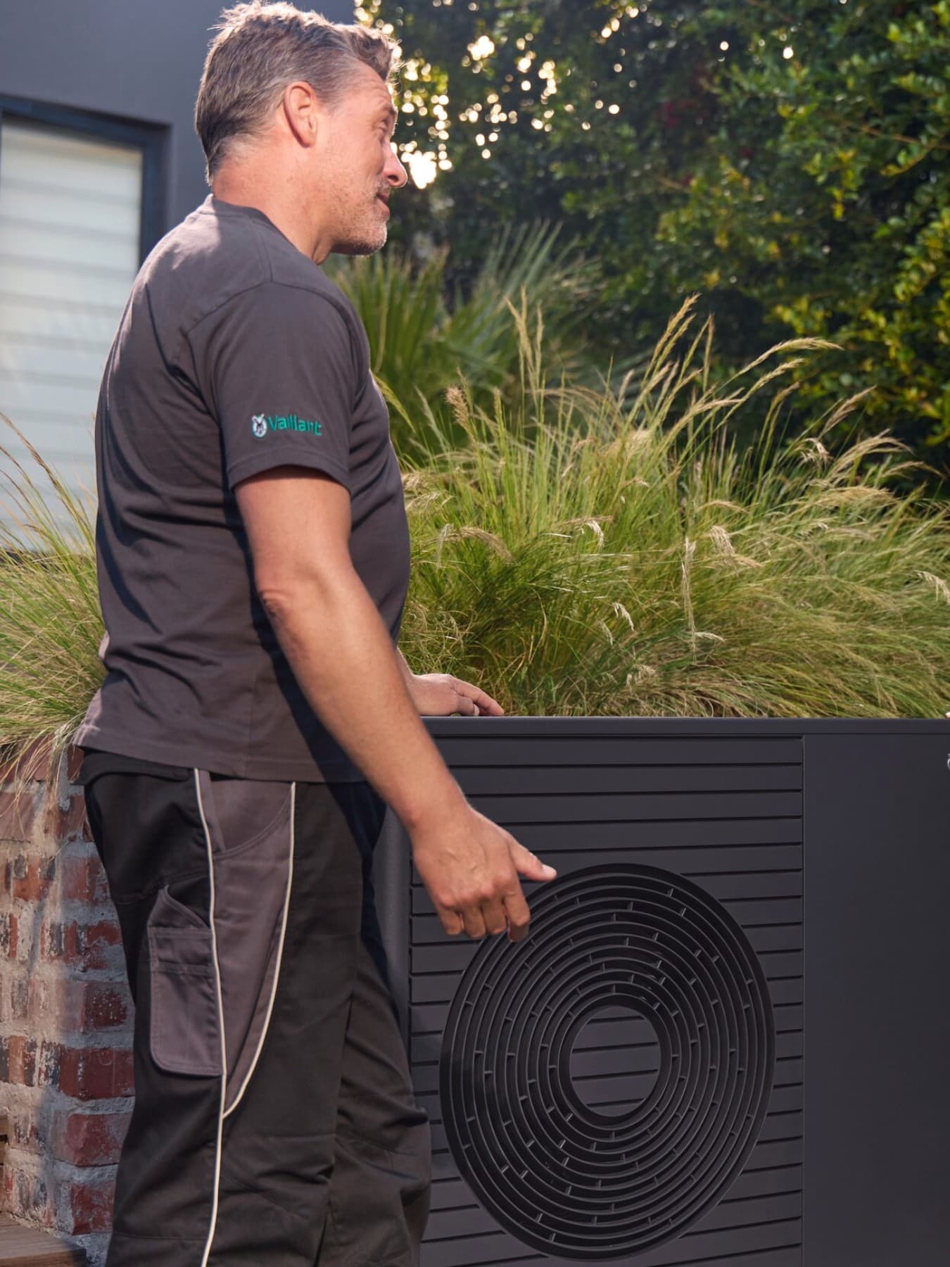 Un installateur de pompe à chaleur et une propriétaire discutant à côté d'une pompe à chaleur | Vaillant