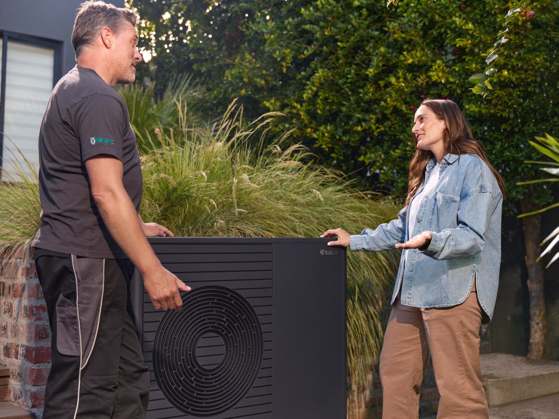 Un installateur de pompe à chaleur et une propriétaire discutant à côté d'une pompe à chaleur | Vaillant