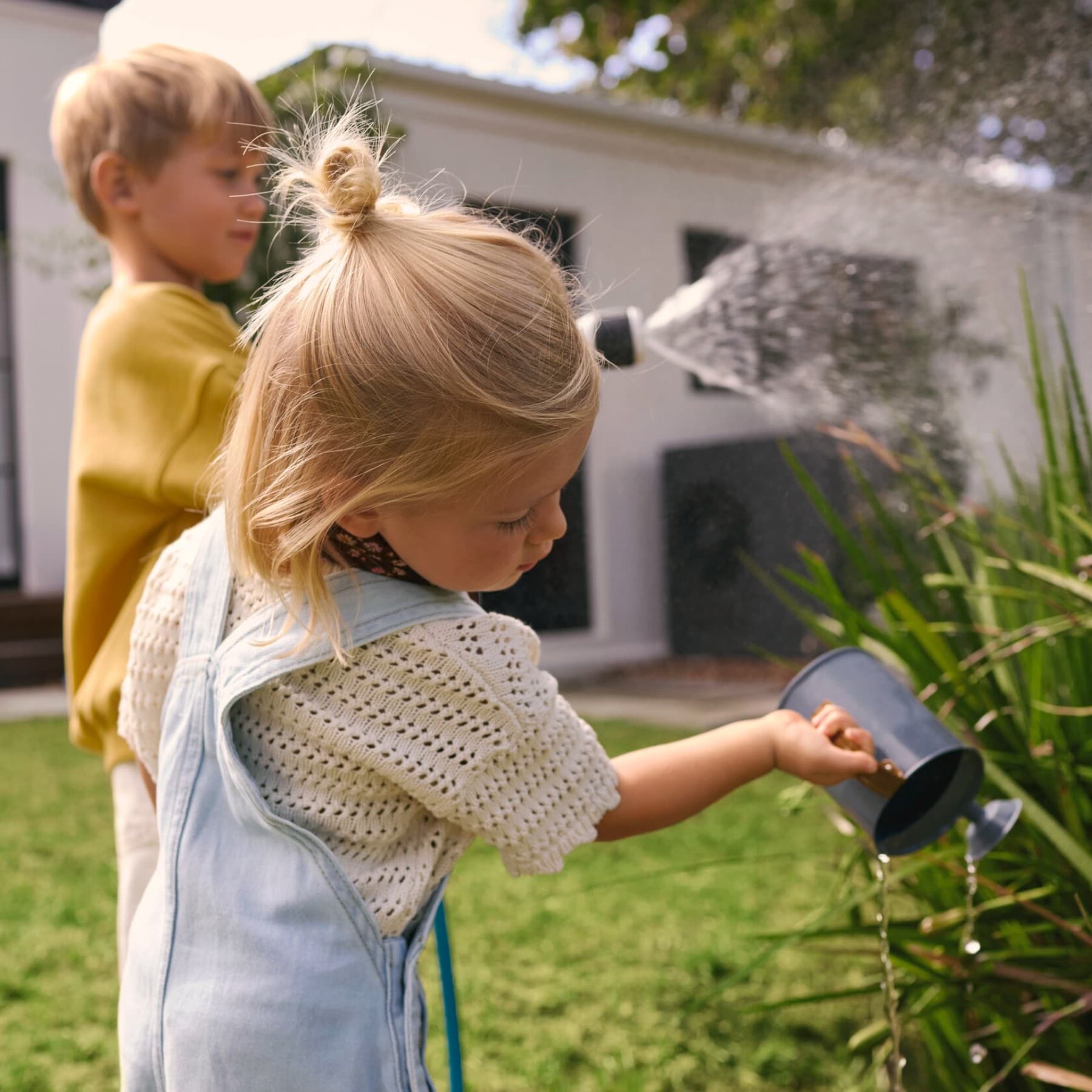 Des enfants arrosent des plantes dans un jardin avec une pompe à chaleur en arrière-plan | Vaillant