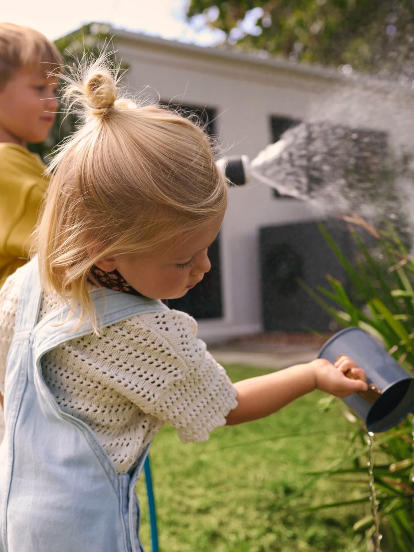 Des enfants arrosent des plantes dans un jardin avec une pompe à chaleur en arrière-plan | Vaillant