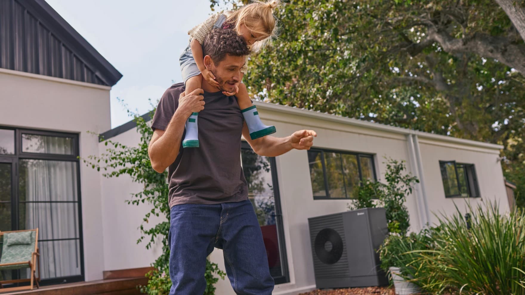 Un père et sa fille devant une unité extérieure de pompe à chaleur dans un jardin | Vaillant