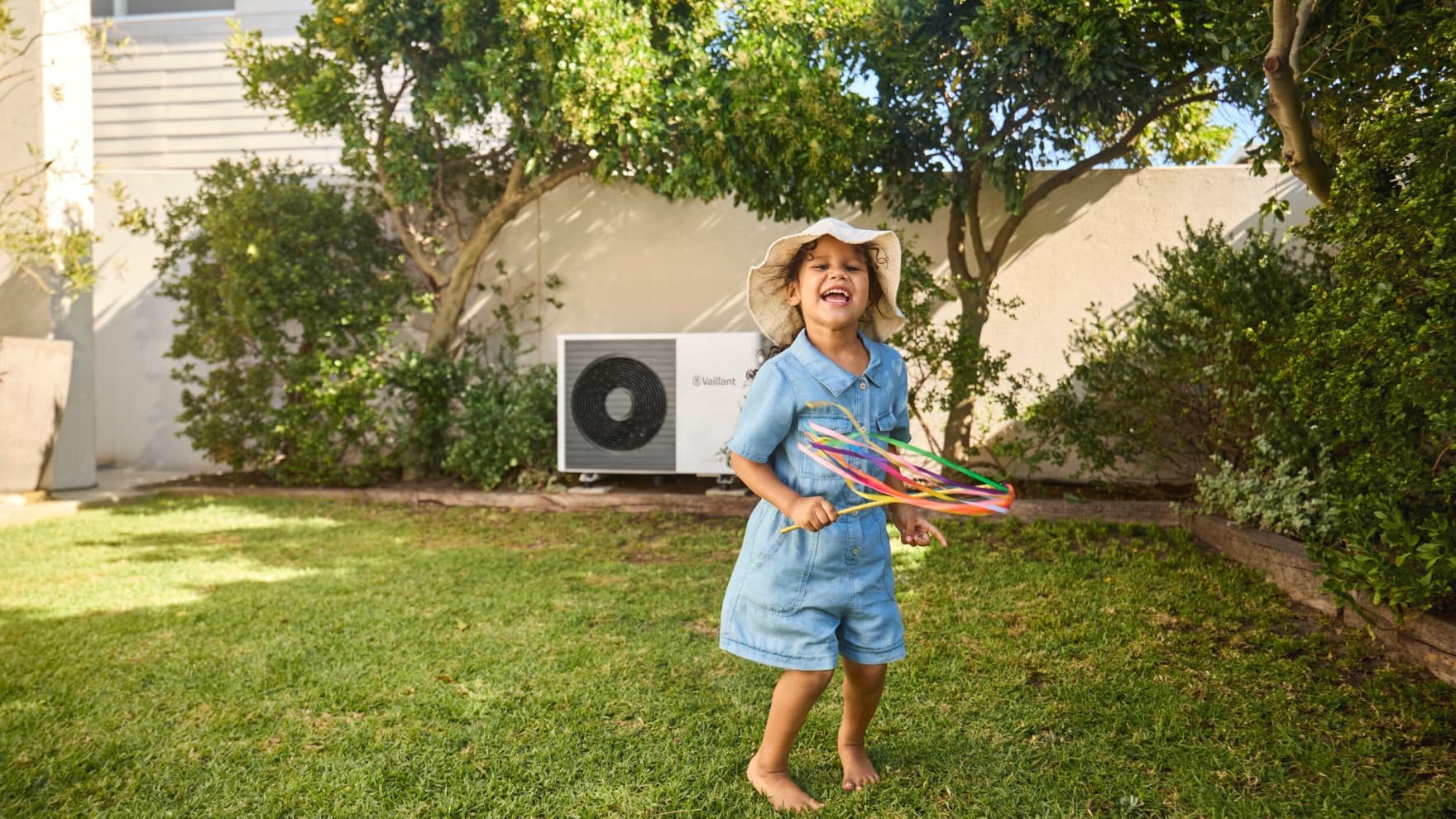 Petite fille jouant dans sont jardin avec une pompe à chaleur en fond | Vaillant