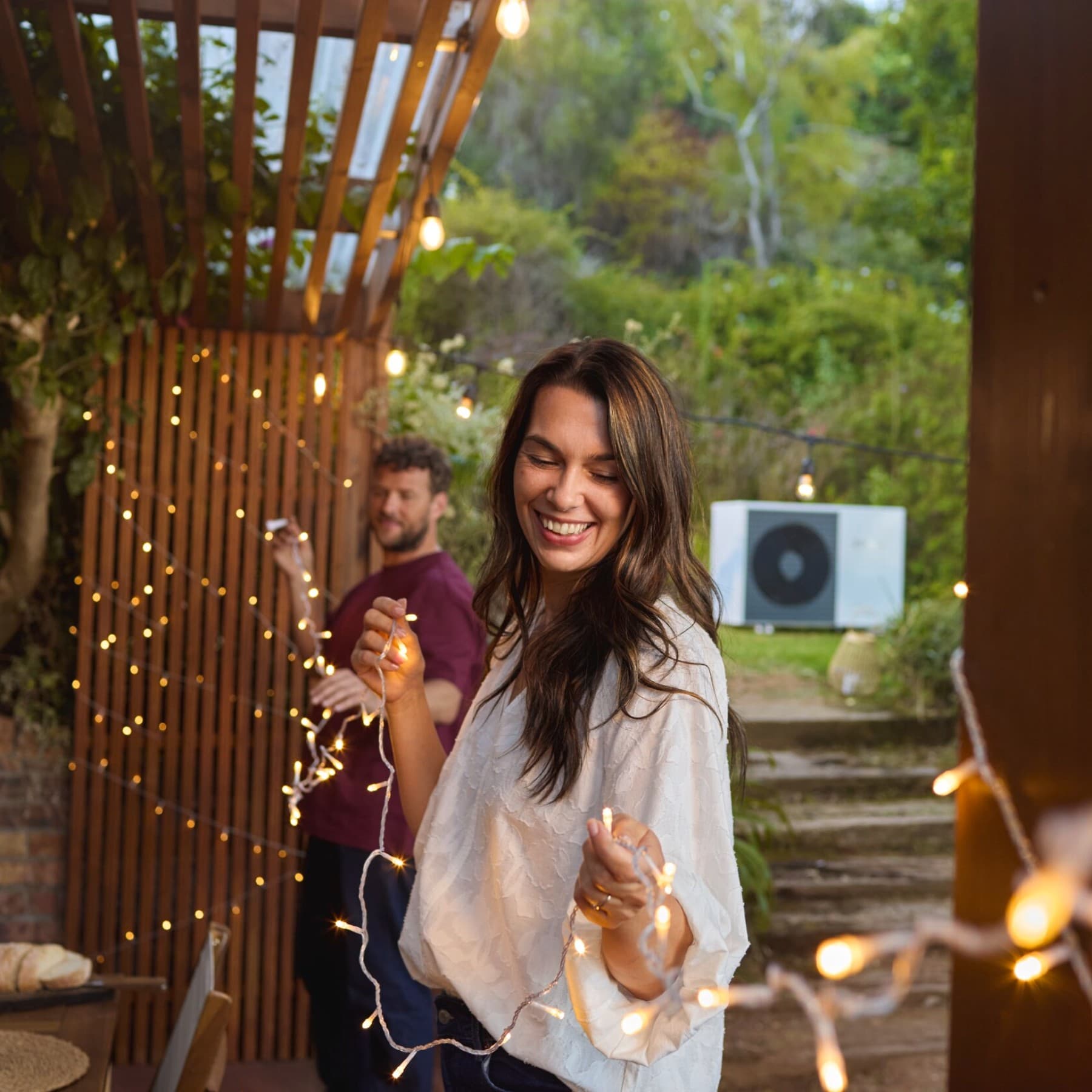 Couple accrochant des guirlandes lumineuses dans le jardin | Vaillant
