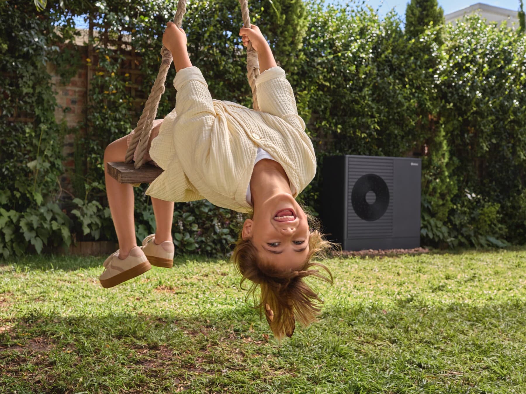 Une jeune fille jouant à la balançoire avec une pompe à chaleur dans le jardin | Vaillant