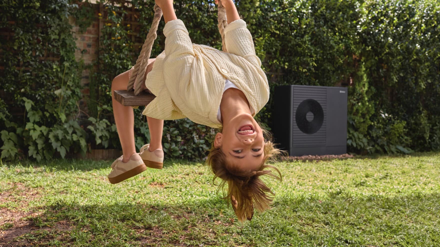 Petite fille faisant de la balançoire dans son jardin avec une pompe à chaleur en fond | Vaillant
