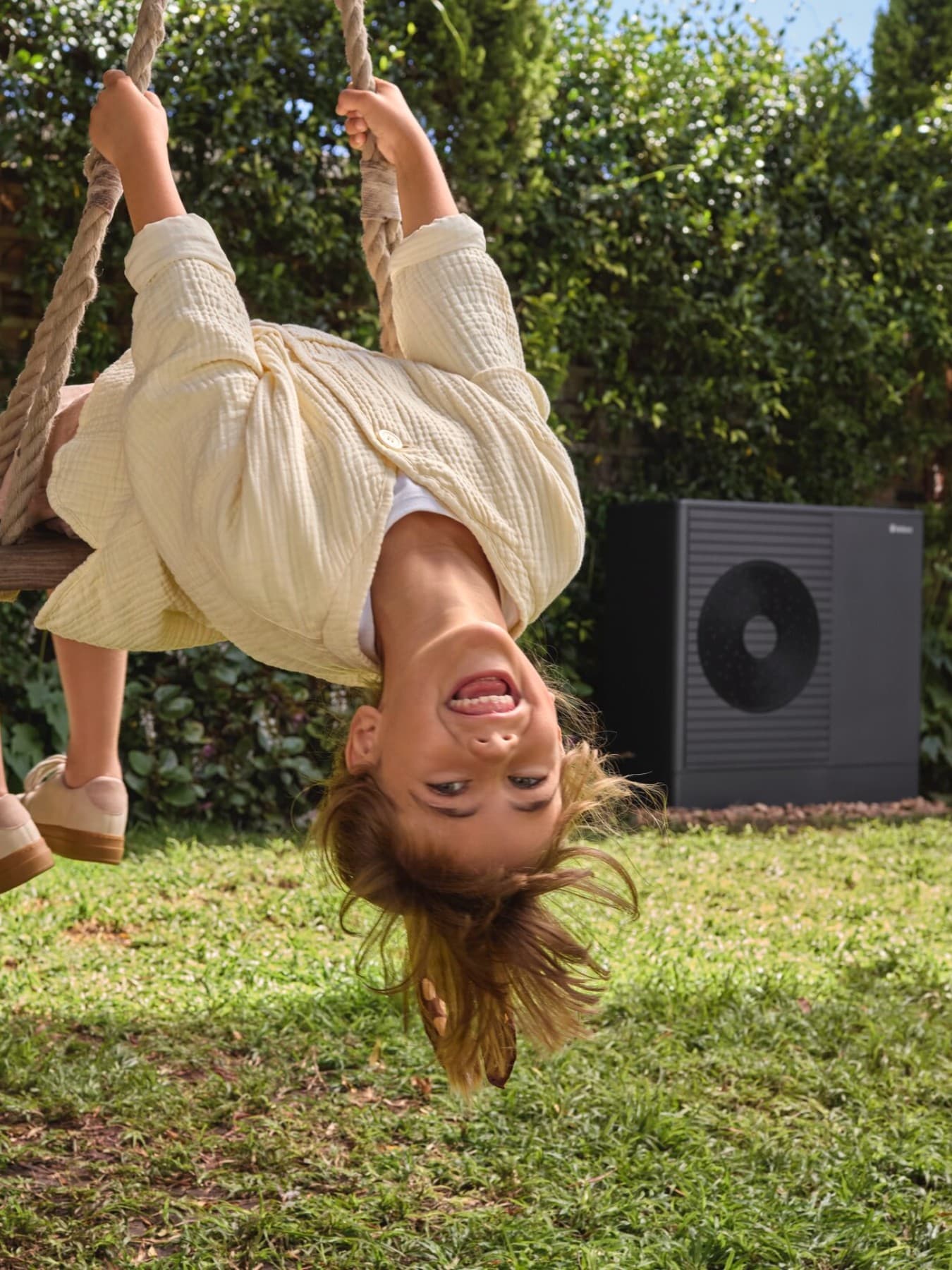 Petite fille faisant de la balançoire dans son jardin avec une pompe à chaleur en fond | Vaillant