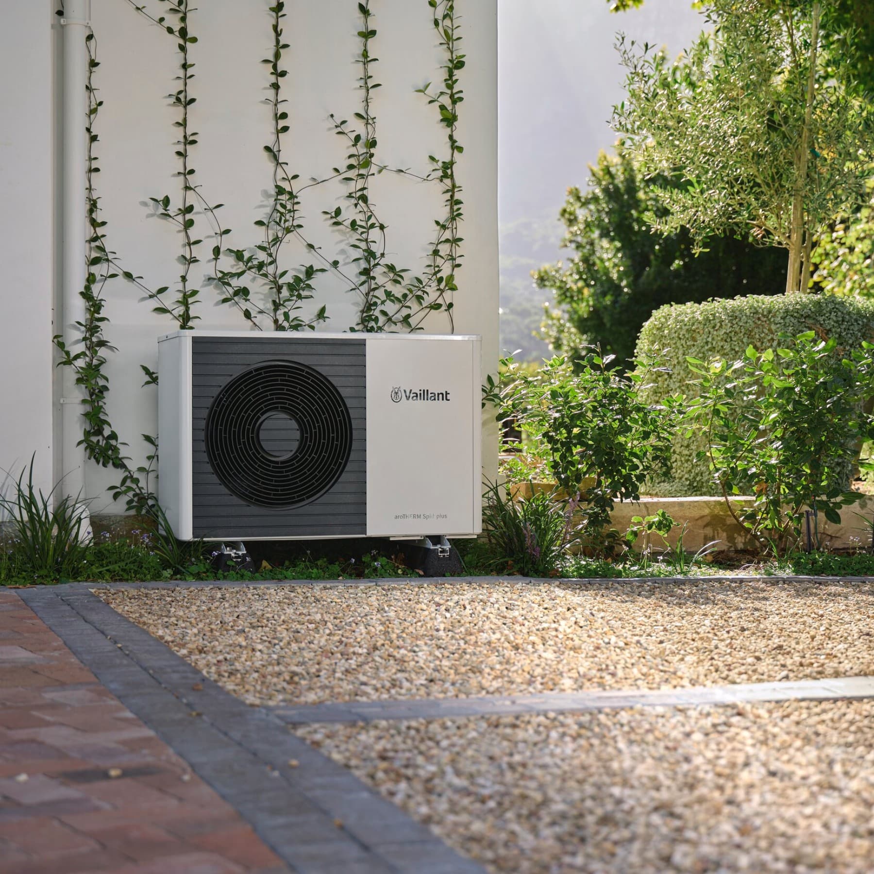 Une unité extérieure de pompe à chaleur dans un jardin sur des gravillons | Vaillant