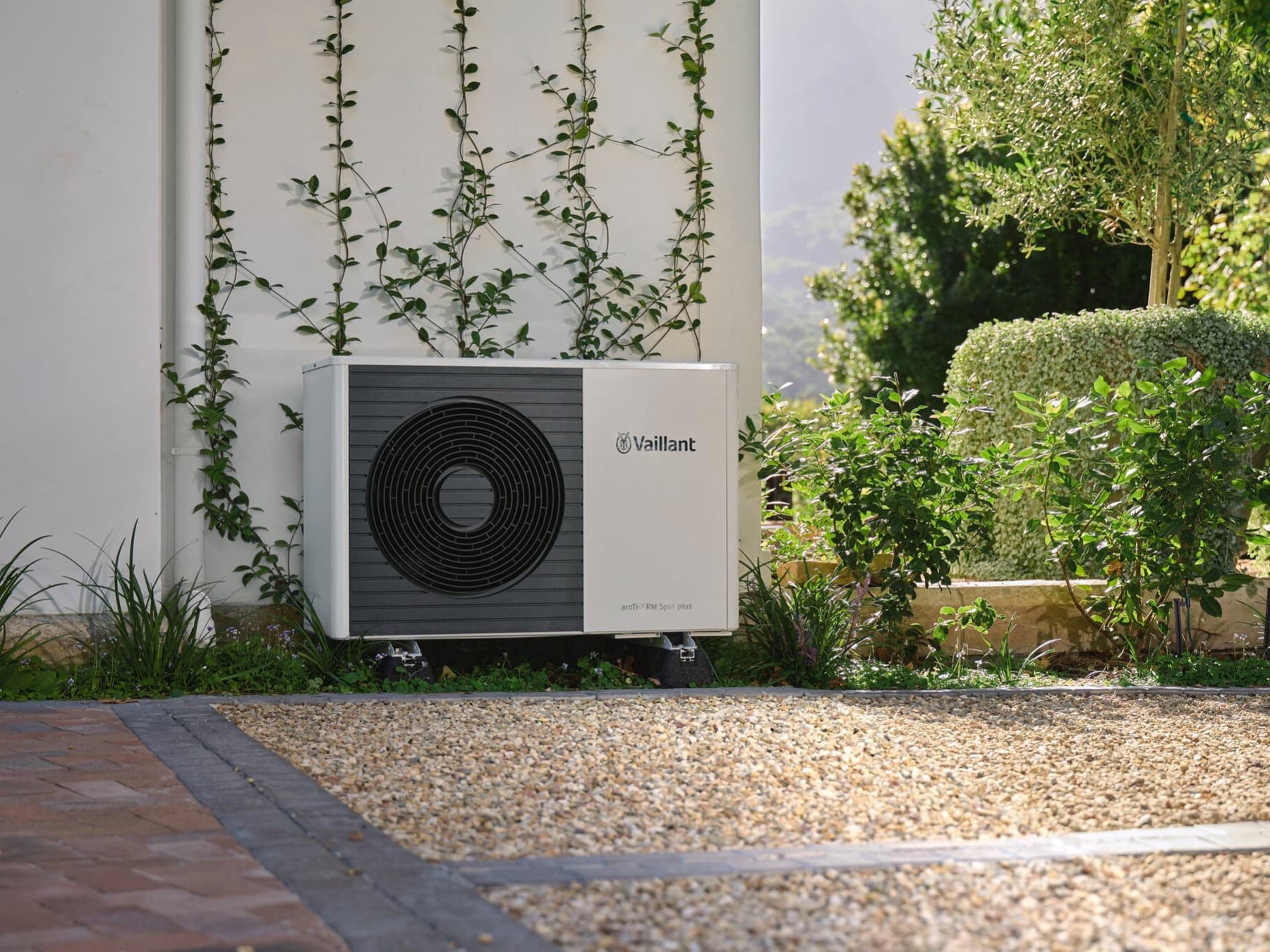 Une unité extérieure de pompe à chaleur installée dans un jardin le long d'une maison | Vaillant