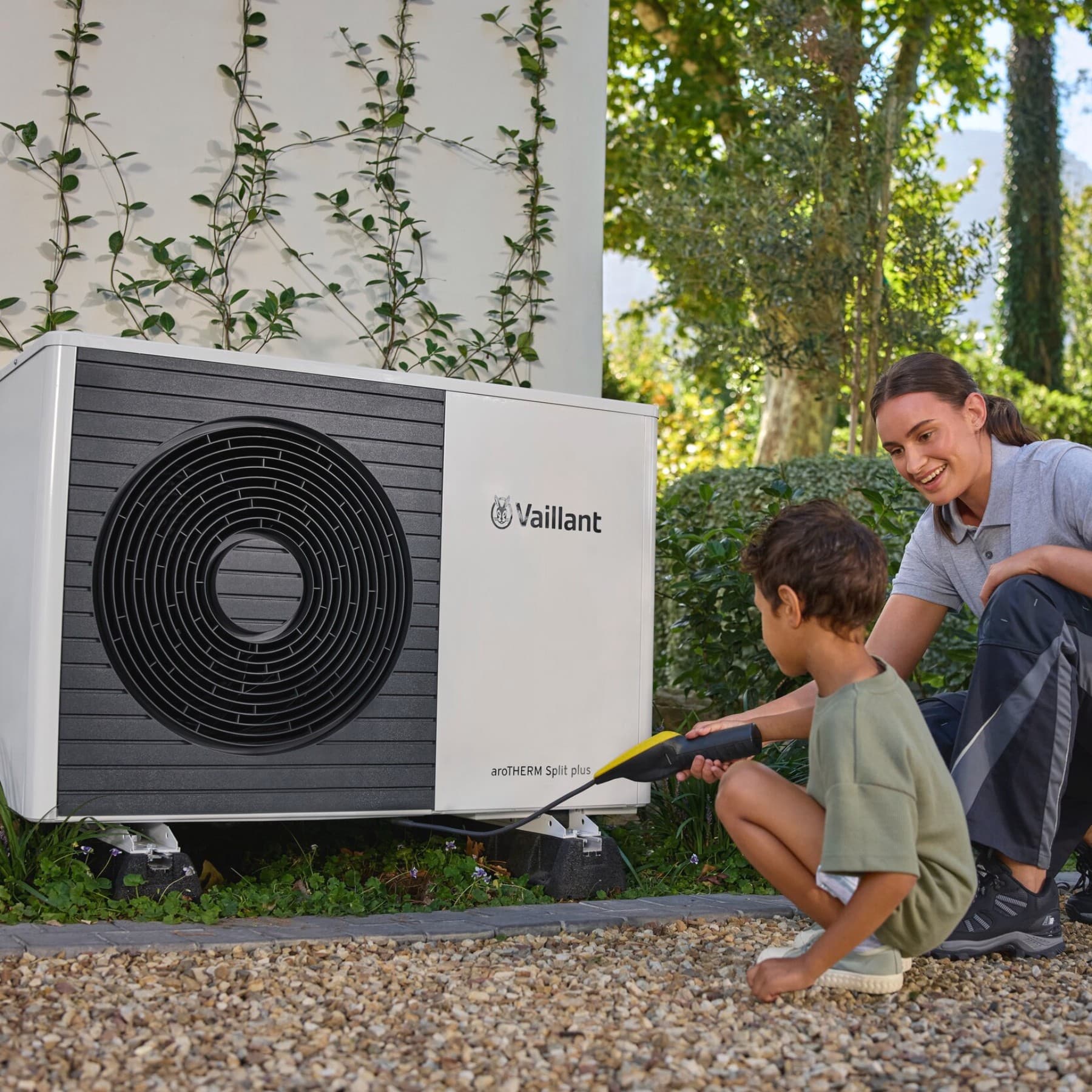 Installateur et enfant devant la pompe à chaleur | Vaillant