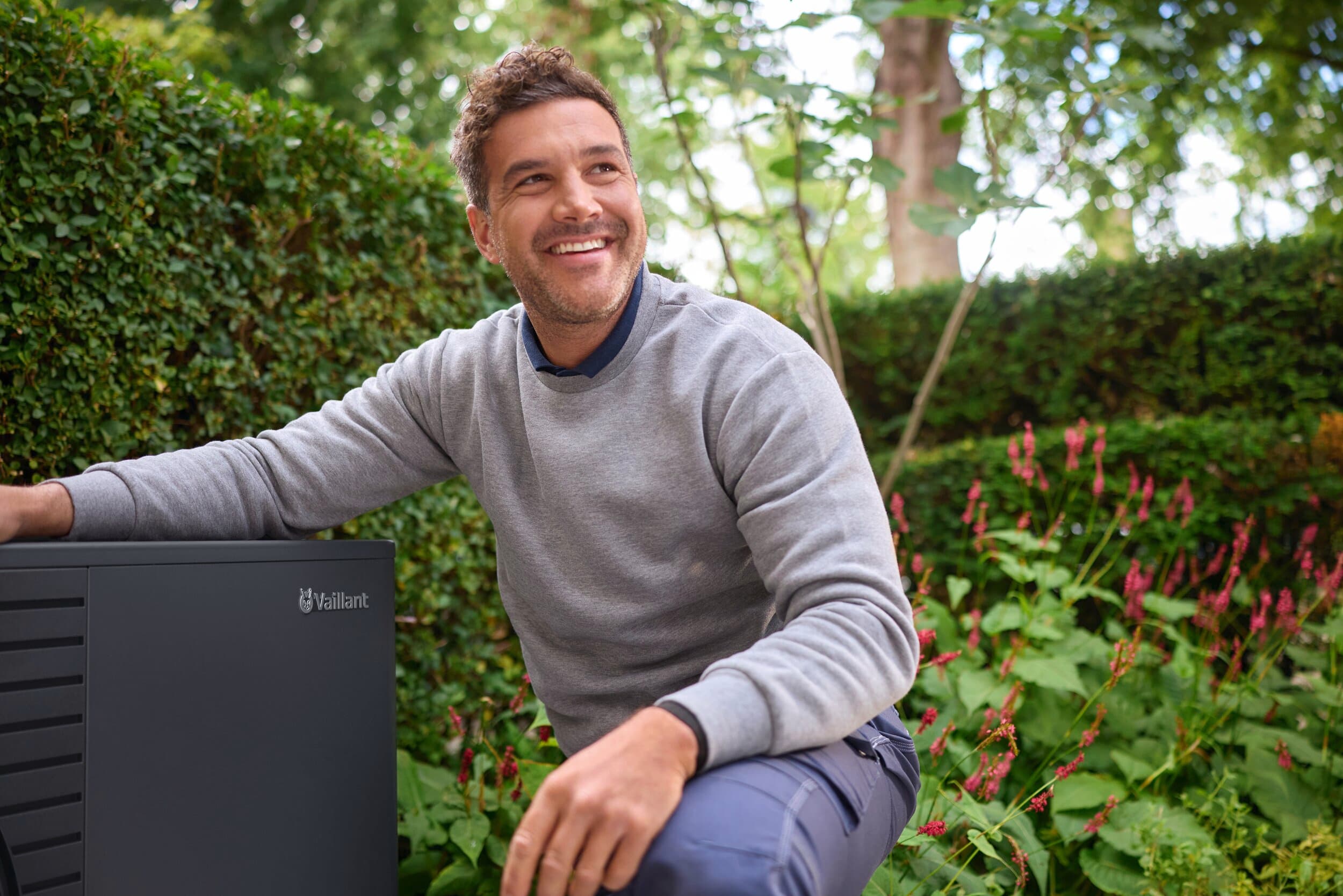 Un homme agenouillé à côté d'un aroTHERM pro dans le jardin | Vaillant