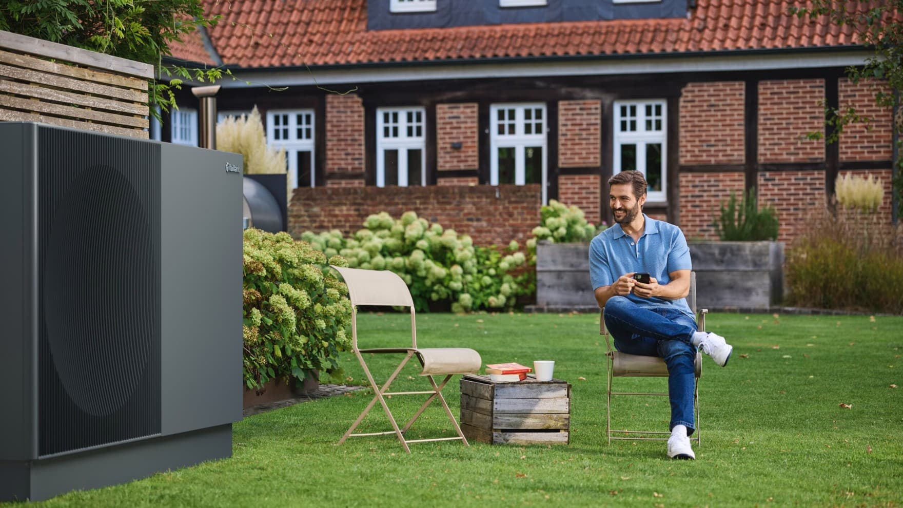 Homme assis sur sa chaise avec son téléphone à côté de aroTHERM perform | Vaillant