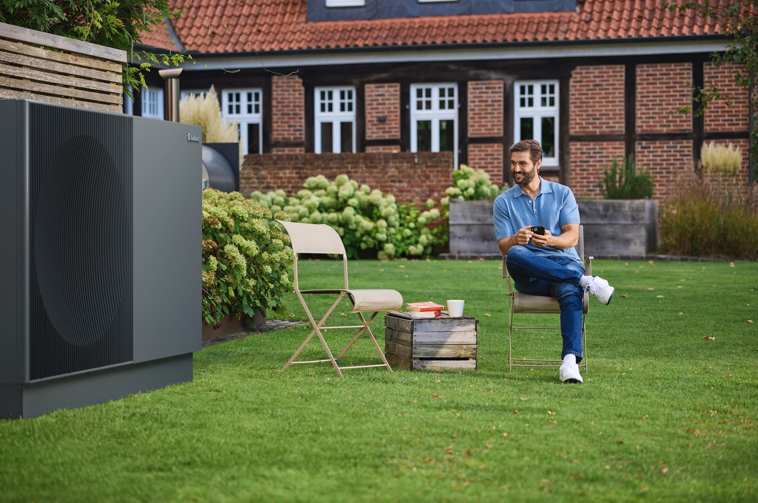 Homme assis sur une chaise dans son jardin près d'aroTHERM perform | Vaillant