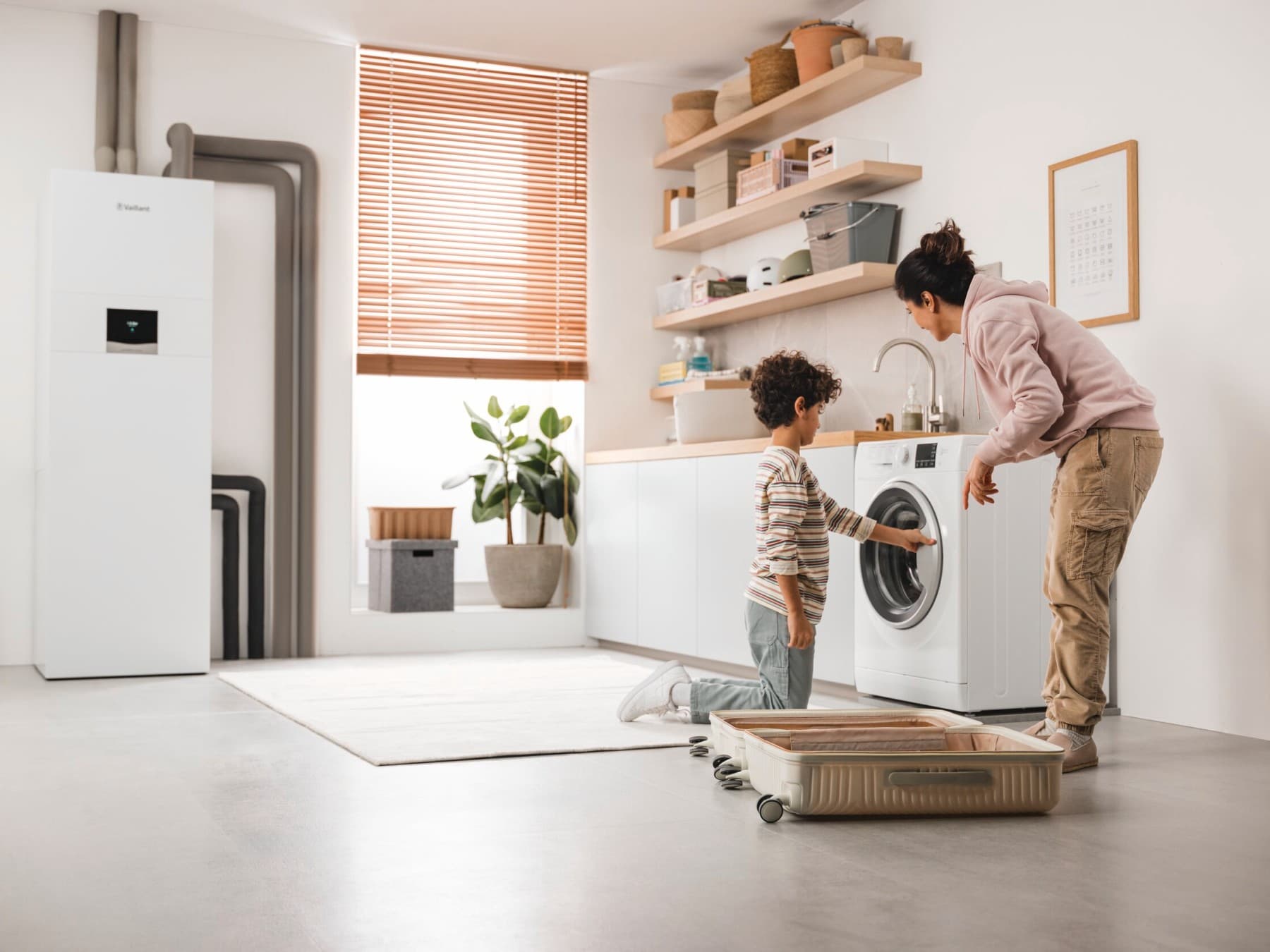 Une mère et son fils vérifiant la machine à laver avec une pompe à chaleur géothermique en arrière-plan | Vaillant